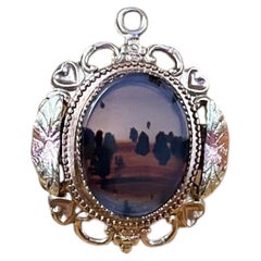 Colgante vintage en tono dorado, en miniatura, con forma de paisaje y un marco de filigrana muy elaborado.