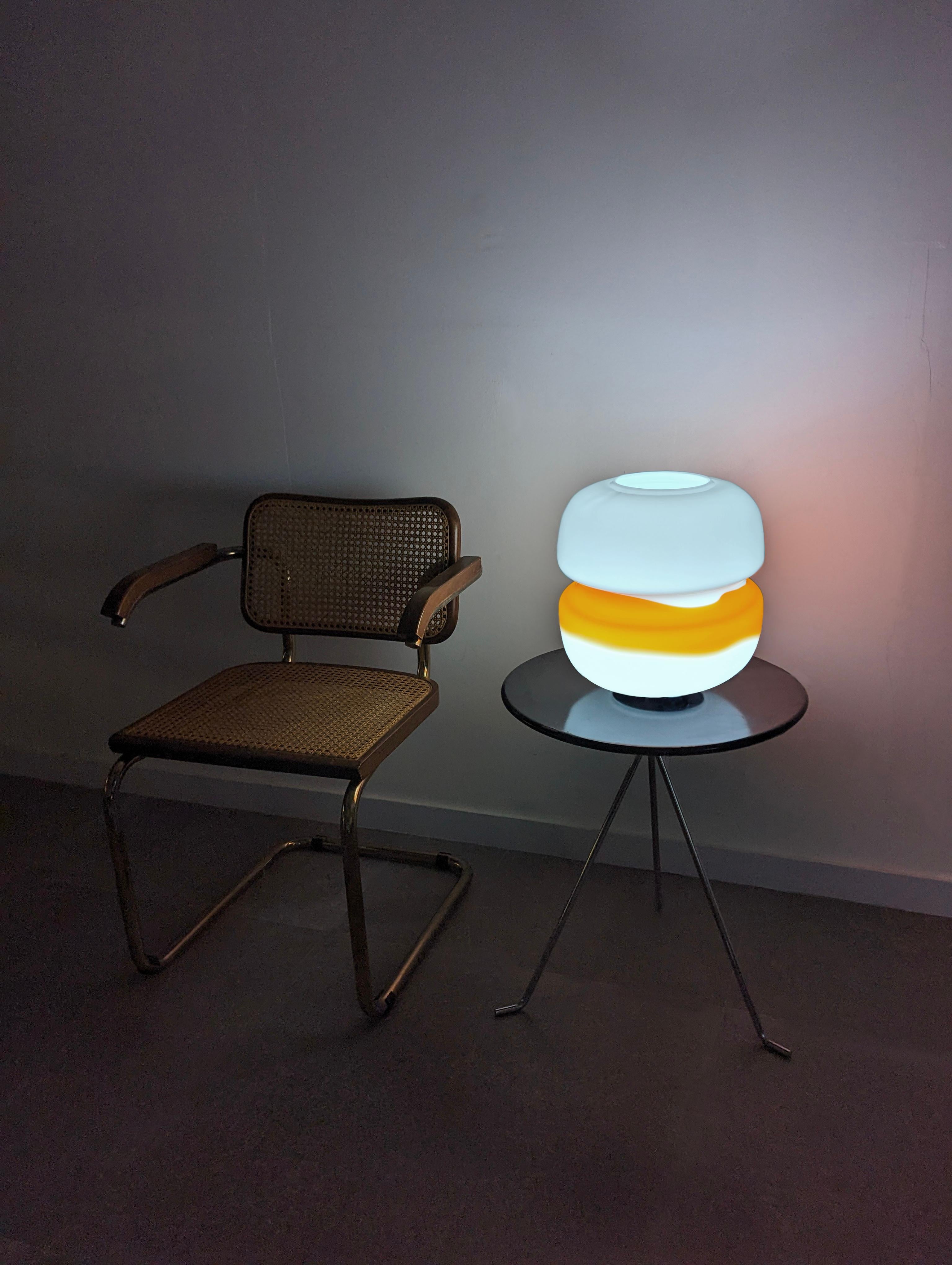 Italian table lamp by Mazzega made in the 70s in white and orange glass with a striking transversal line design. Once turned on, its colors provide a warm and elegant atmosphere.
