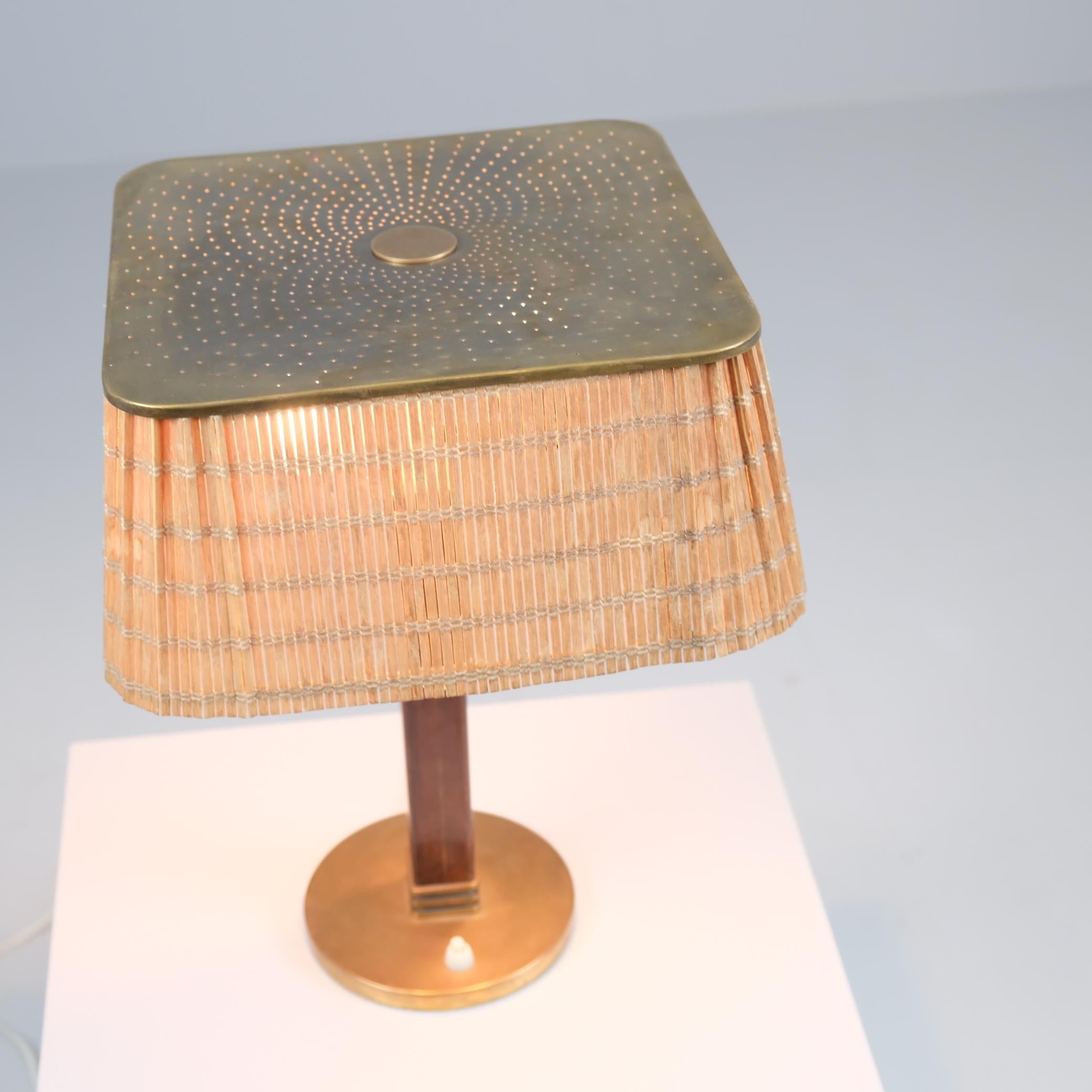 Esta lámpara de mesa, Model No. 5066 de Paavo Tynell para Taito Oy de los años 50 es un clásico. Tiene un soporte redondo de latón, una pata de madera dura y una hermosa pantalla de ratán color caoba claro de líneas limpias. La parte superior de la