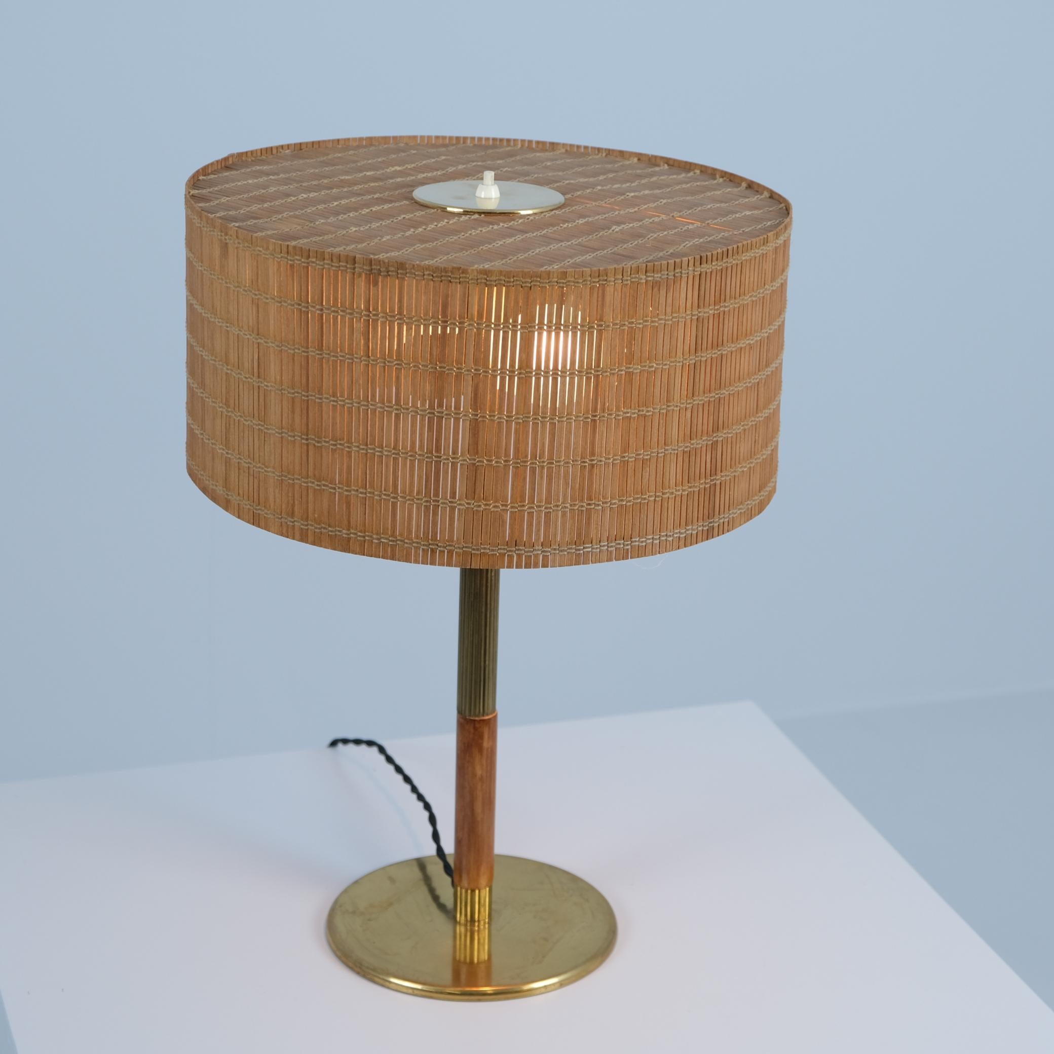 Lámpara de mesa Paavo Tynell modelo 5068, fabricada por Taito Oy en los años 50, excelente estado. Se trata de una versión poco frecuente con una pata de latón ranurada que sujeta una pieza de abedul como asa al mover la lámpara. La lámpara está en