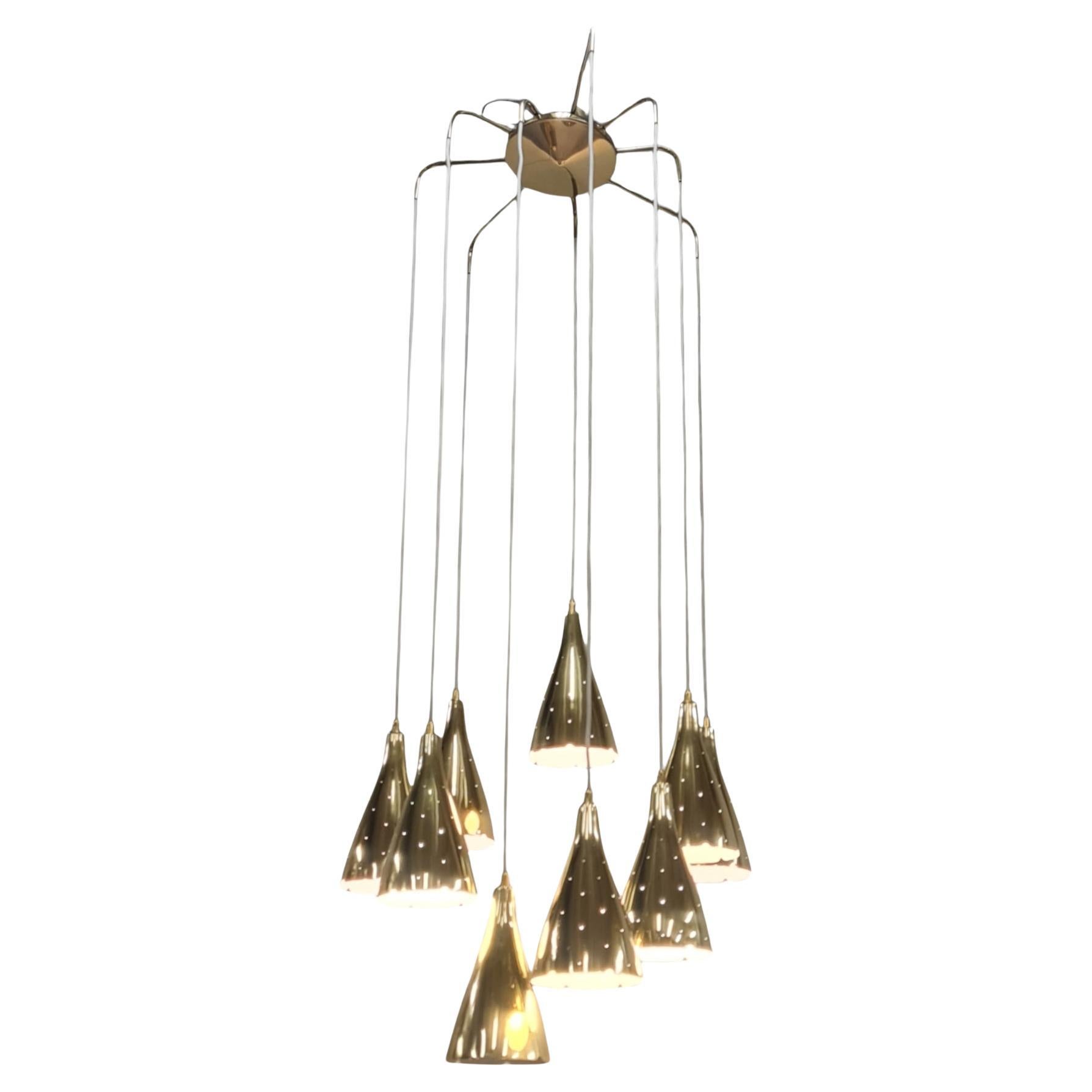 A sizable ceiling light by Paavo Tynell with nine hanging perforated brass pendants connected at the top with a brass central piece with radiating arms of different lengths. The pendants themselves hang at different heights and can also be adjusted