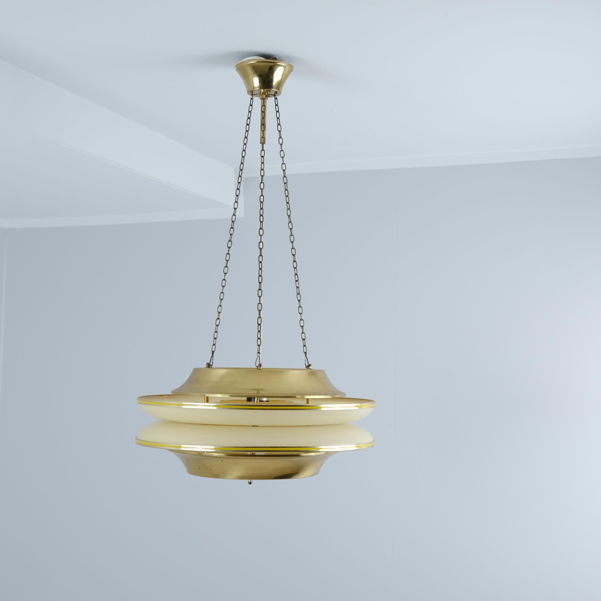 Una sospensione da soffitto a lamelle modernista del designer finlandese Kai Ruokonen (Finnmark), composta da due lamelle di ottone contrapposte che racchiudono due dischi acrilici beige convace che fungono da diffusore di luce. Un pezzo futuristico