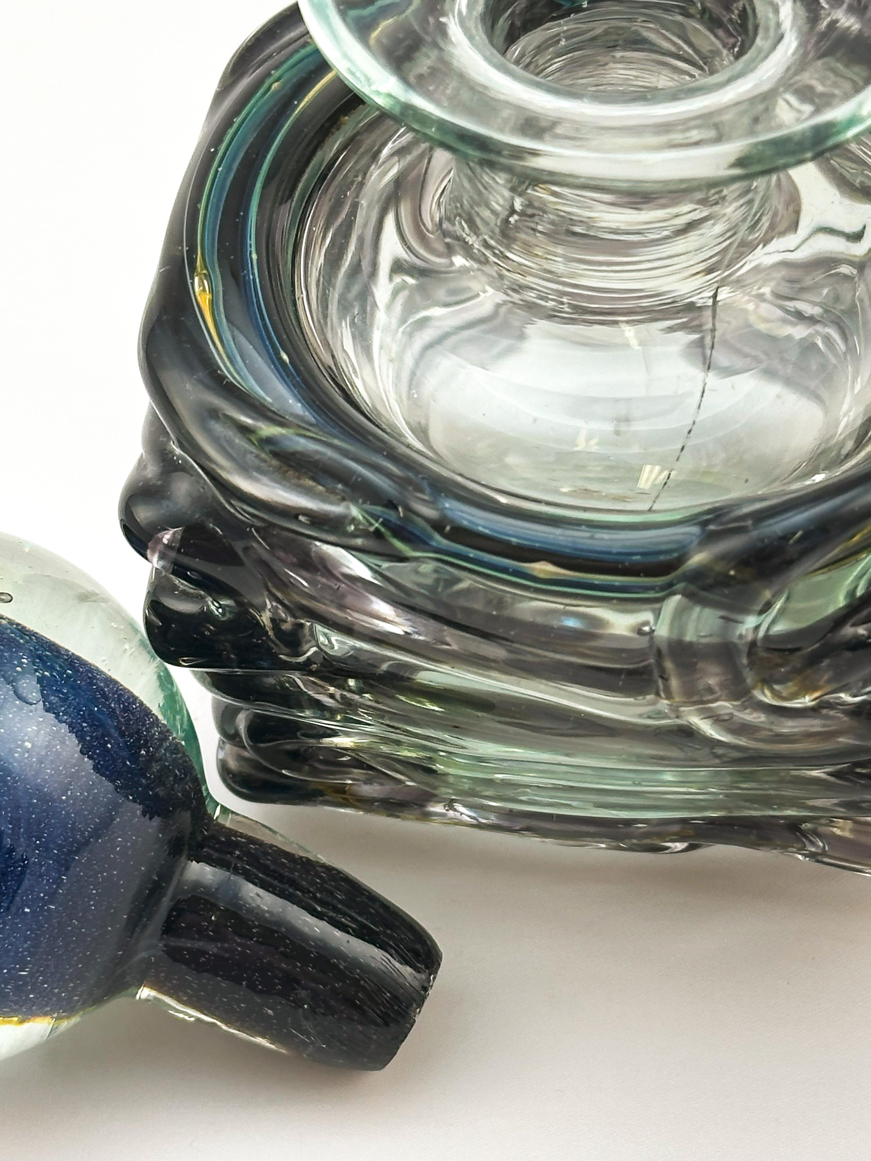 Questa bottiglia di profumo vintage di Mdina Glass è stata realizzata a Malta negli anni '70 e riflette l'approccio distintivo dello studio al design del vetro artistico. La bottiglia presenta un corpo quadrato in vetro traslucido grigio-blu,