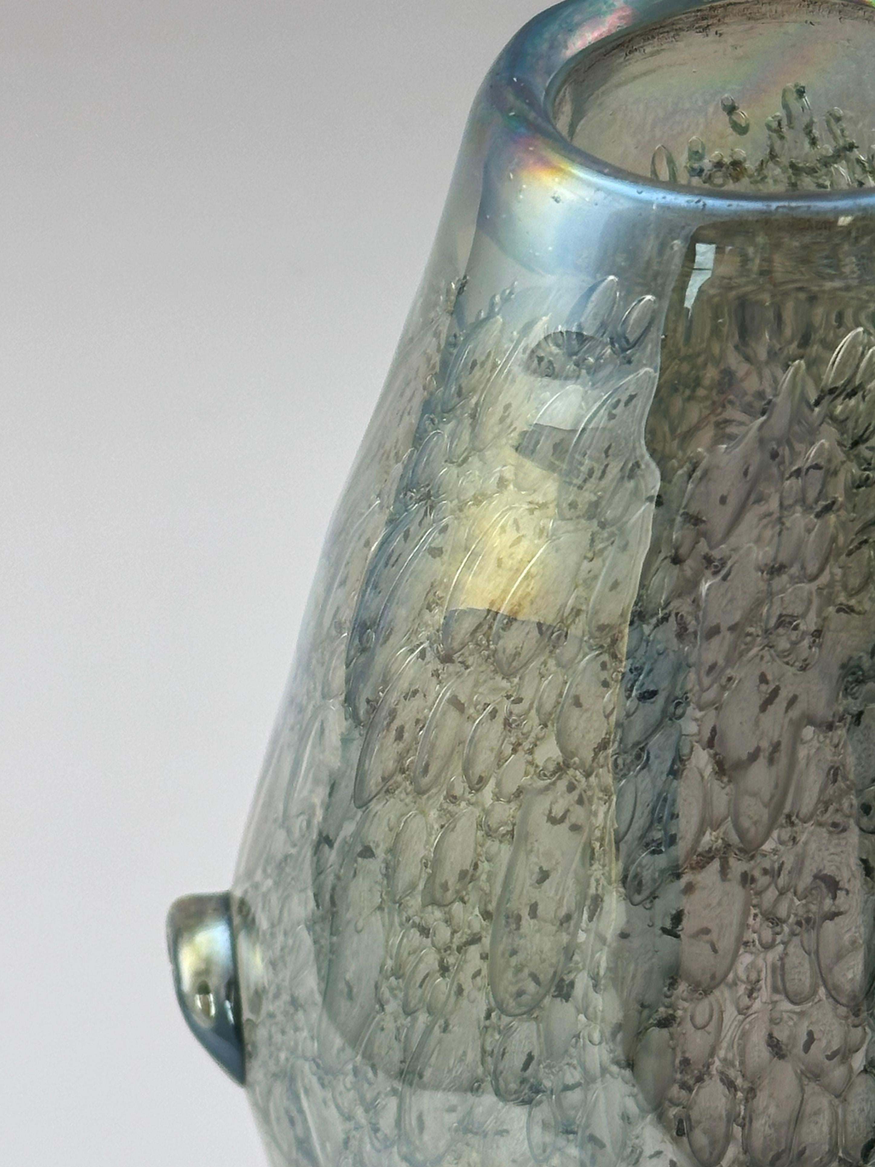 This iridescent Murano-style glass vase, made in Italy around the 1970s, exemplifies the artistry and technical finesse associated with Italian studio glass. Its distinctive freeform shape echoes a double truncated cone, rendered in thick, luminous