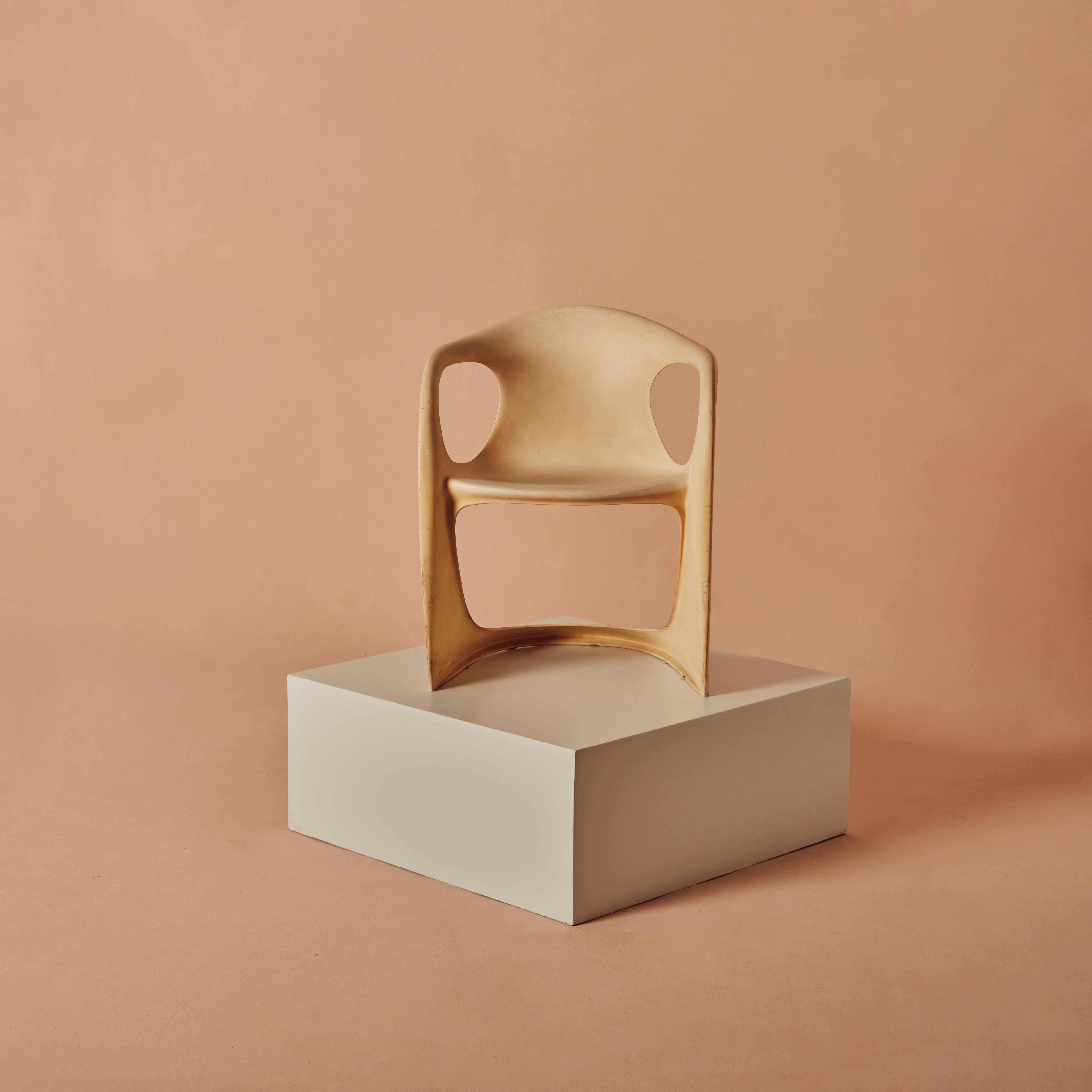 The chair is formed in an organically shaped frame made of eggshell-coloured plastic with armrests, embossed with the manufacturer on the underside.
  