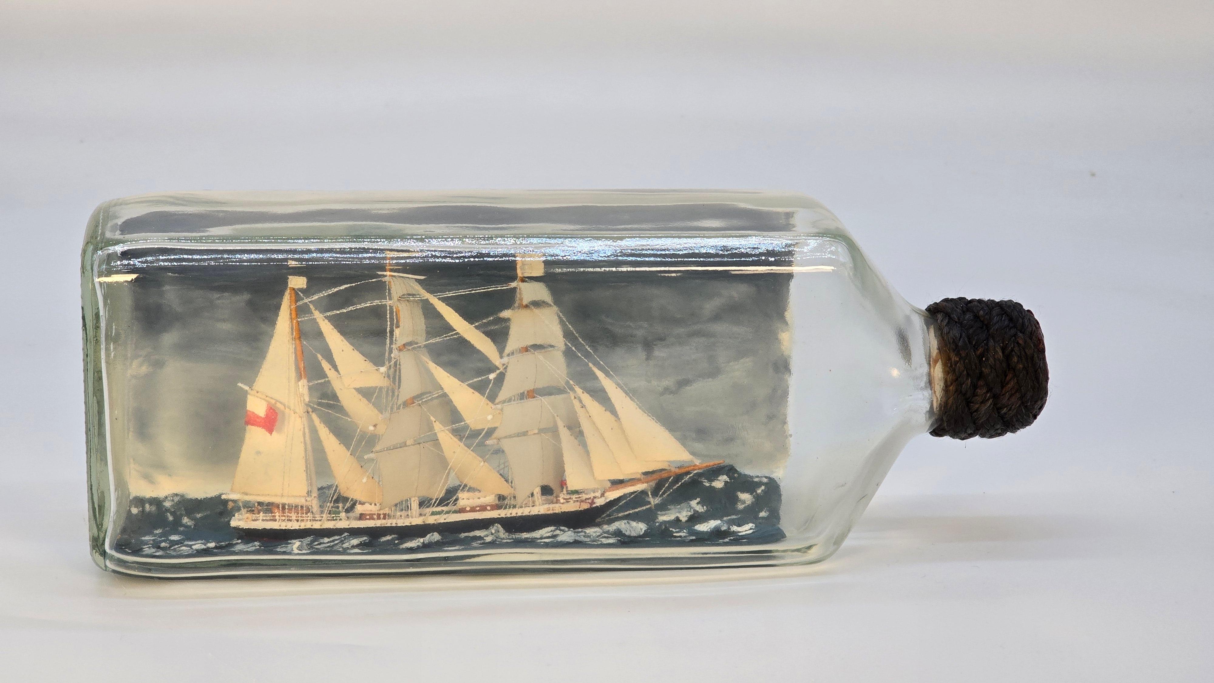This is a very fine example of the art of building a model ship in a glass bottle. It is constructed in a large rectangular whiskey bottle. The ship is a three masted barque named Seamaid circa 1870 and made in Glasgow. It is modelled in full sail