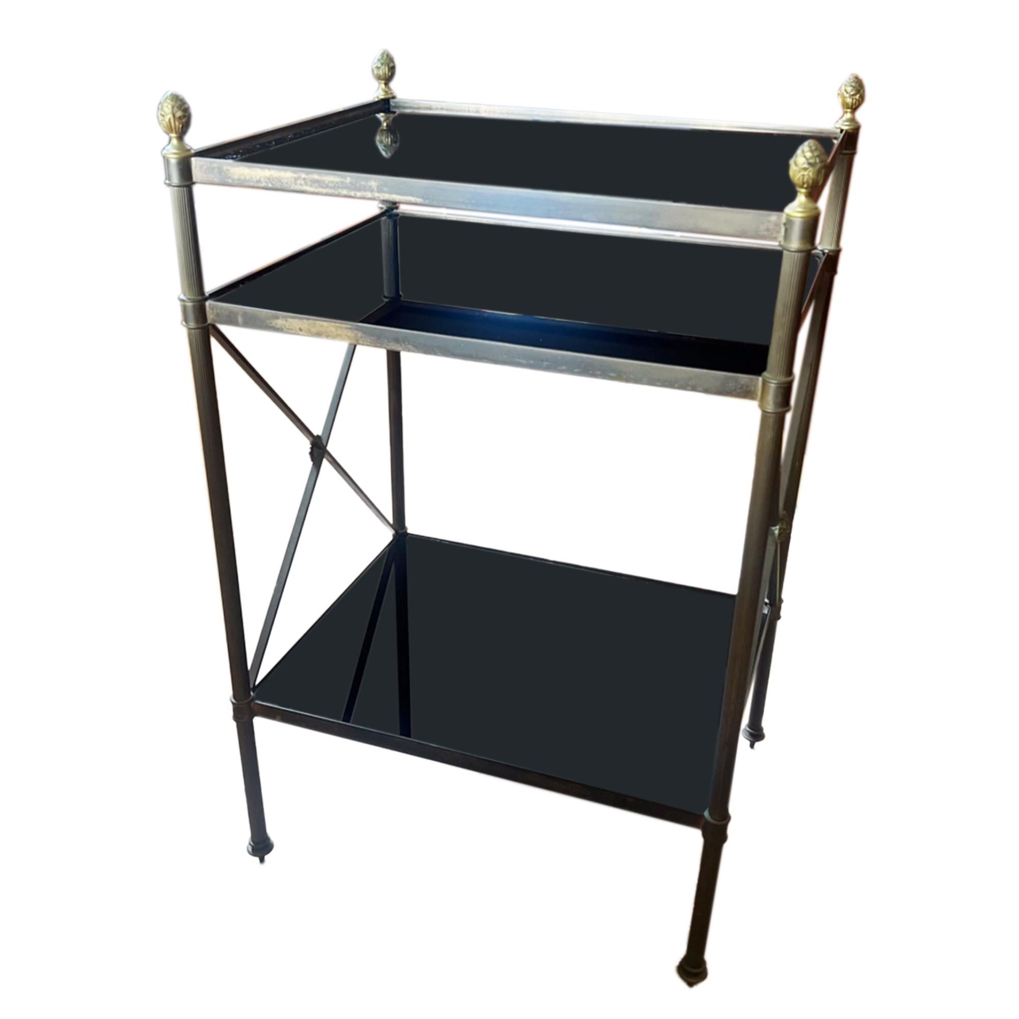 Cette table d'appoint à trois niveaux est fabriquée en laiton et en verre noir stylisé. Elle est décorée d'embouts d'ananas joliment moulés et de pieds cannelés. 

Simple et élégant, cet objet, qui est également pratique, serait un bel ajout à