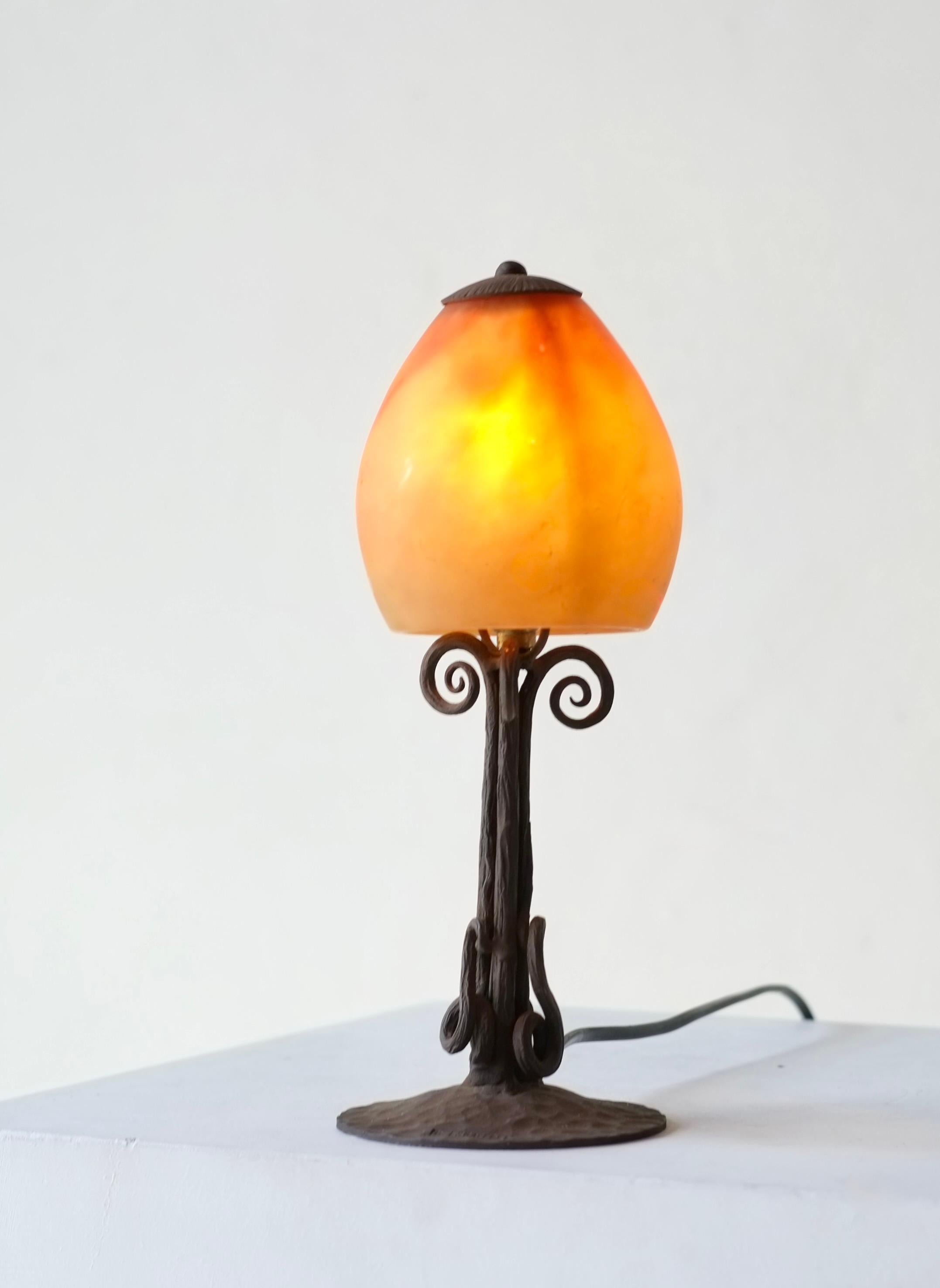 Elegante lámpara de escritorio Art Nouveau de metal forjado y cristal, obra del herrero francés P. Escaffre.

Pantalla de vidrio soplado a mano de doble capa moteada con inclusiones de pigmentos, fabricada por Daum, Nancy.

Firmado 