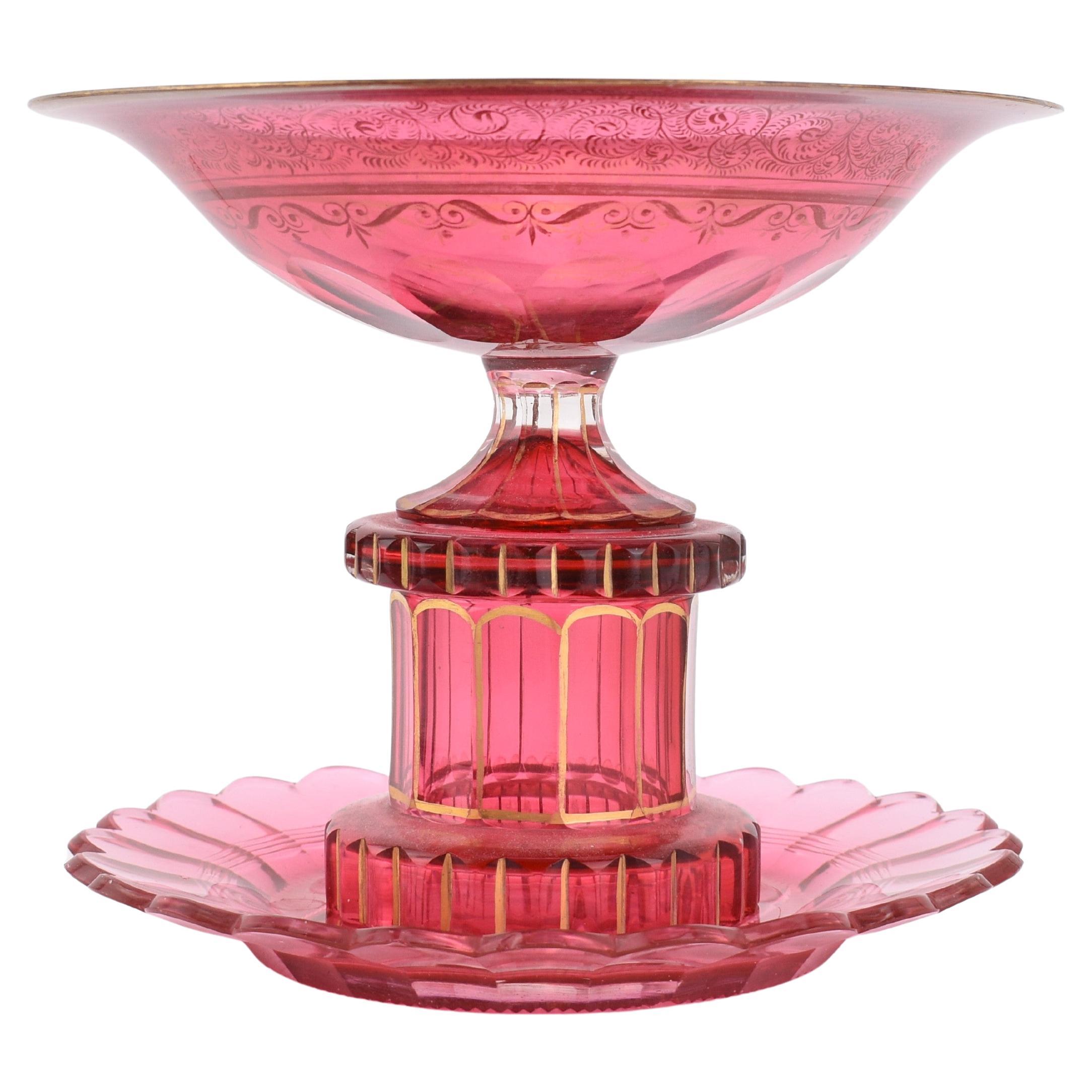 Cranberry glass serving centerpiece by Moser

circular body with rich decoration all around featuring a continuous line of 24 carat matte and burnished gold scrollwork, standing on a 12-sided foot with gilding highlights between the side panels,