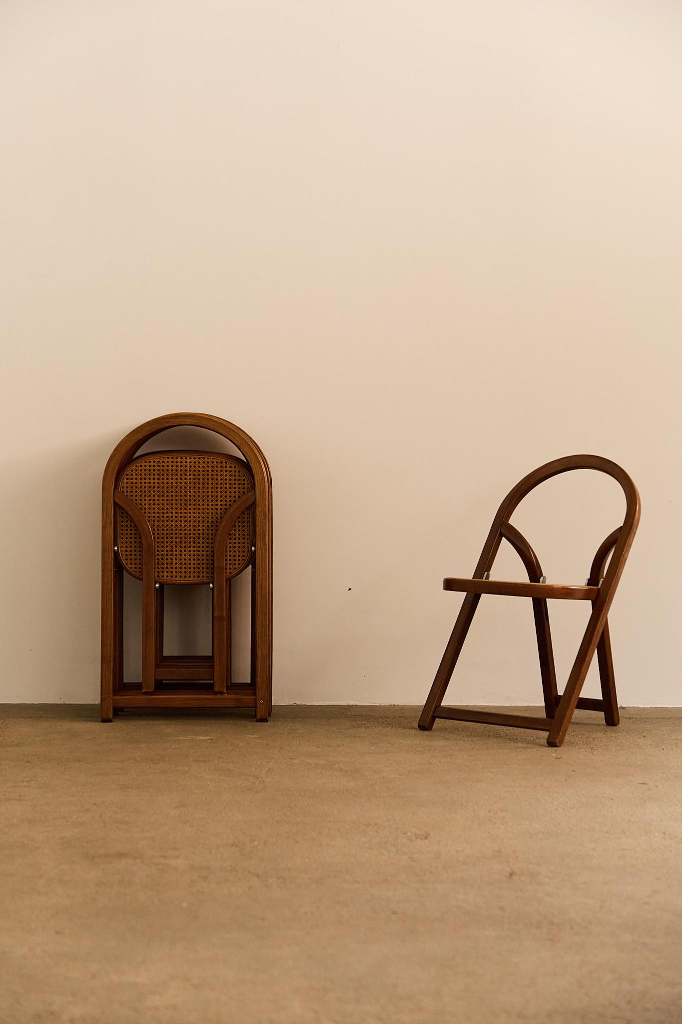 Ein Set aus sechs eleganten, klappbaren Stühlen, entworfen von Gigi Sabadin, die natürliche Geflechtsitze mit fein gearbeiteten Holzrahmen kombinieren. Diese Stühle sind sowohl praktisch als auch stilvoll und spiegeln Sabadins charakteristischen