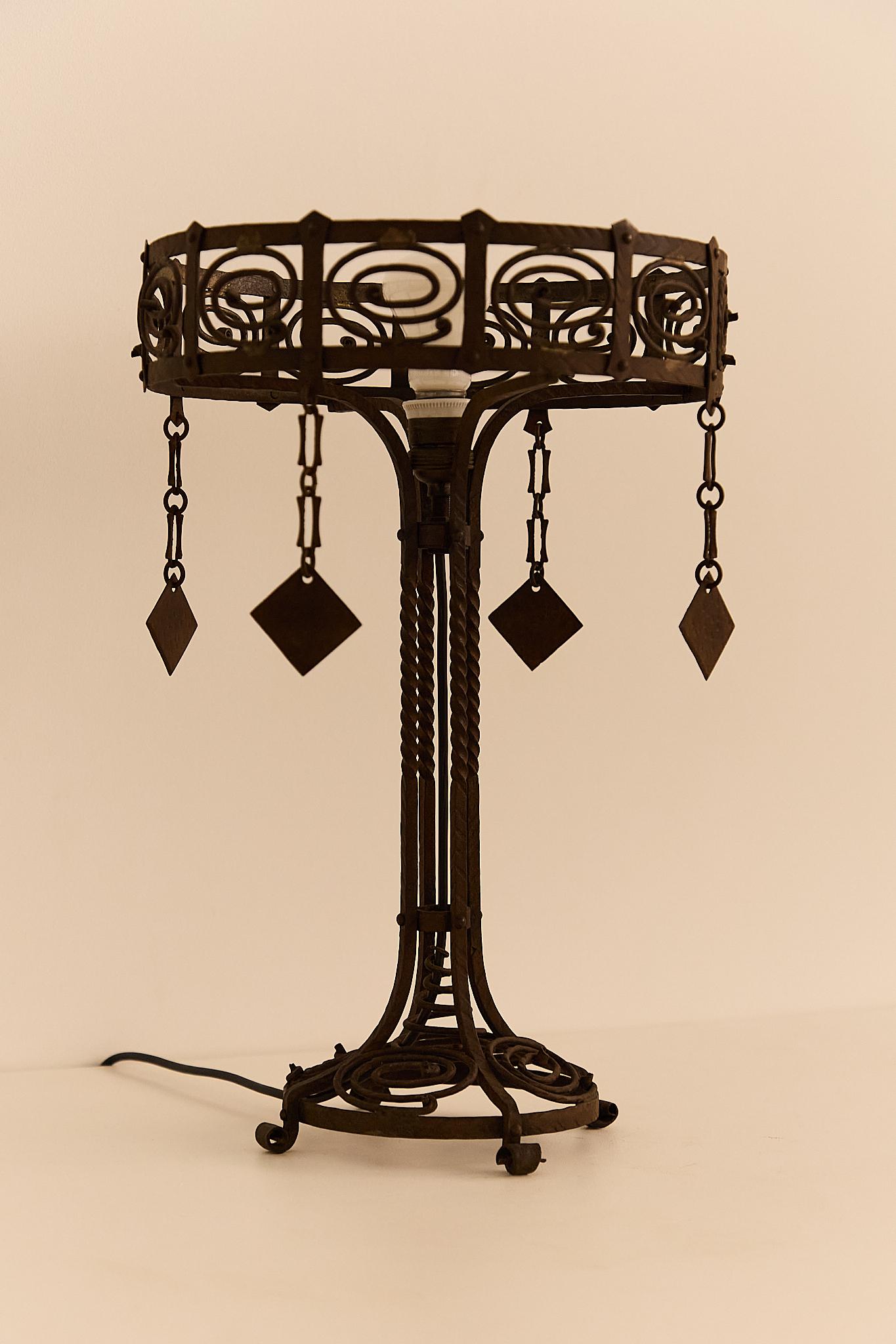 Table lamp in wrought iron, featuring a hat and base adorned with pinwheel motifs and four decorative pendants.