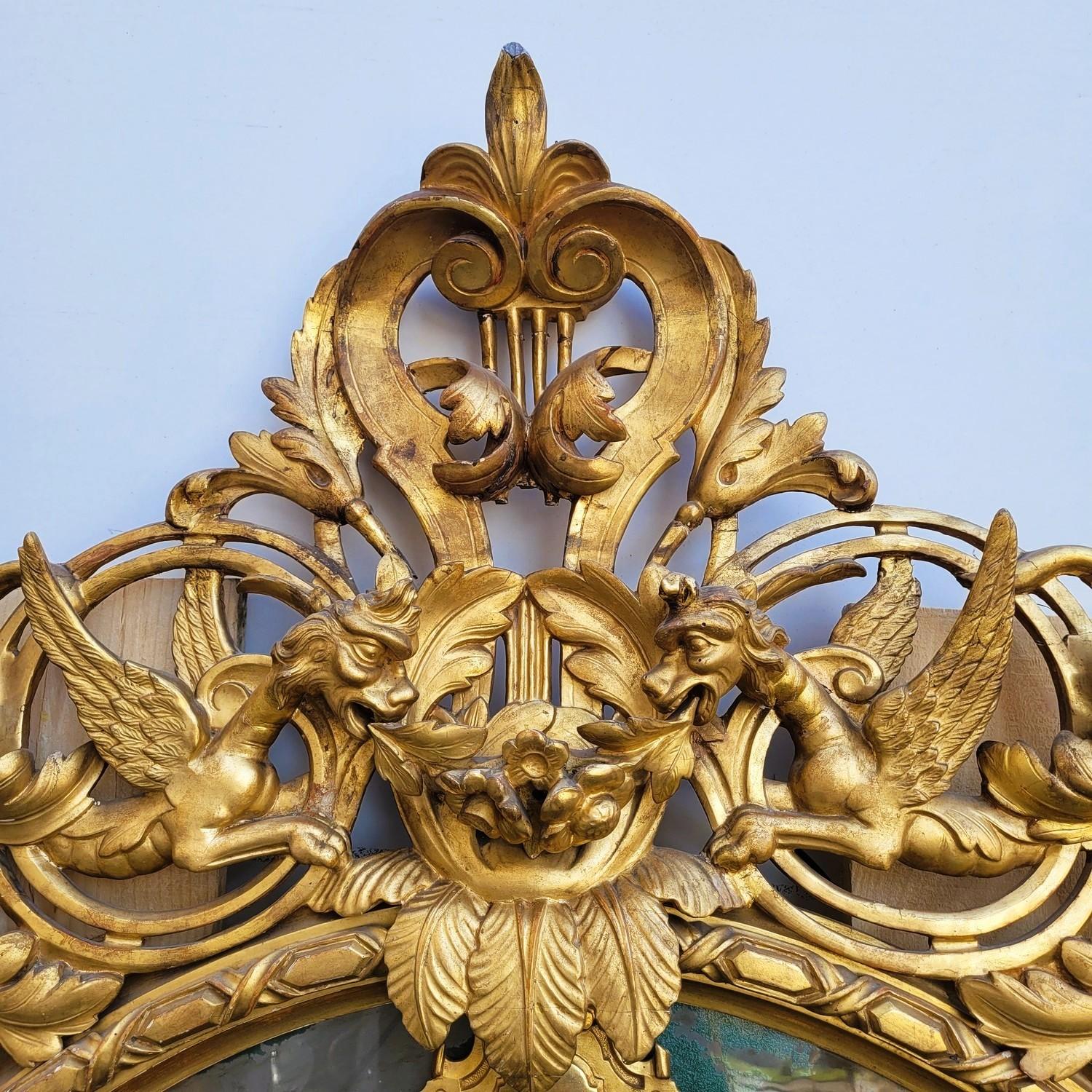 Gran espejo ovalado de madera dorada, con reservas, con frontón ricamente tallado de dragones alados que evolucionan en una decoración de follaje.   

Las reservas tienen una decoración pintada dorada y el fondo debió de estar pintado de verde, hay