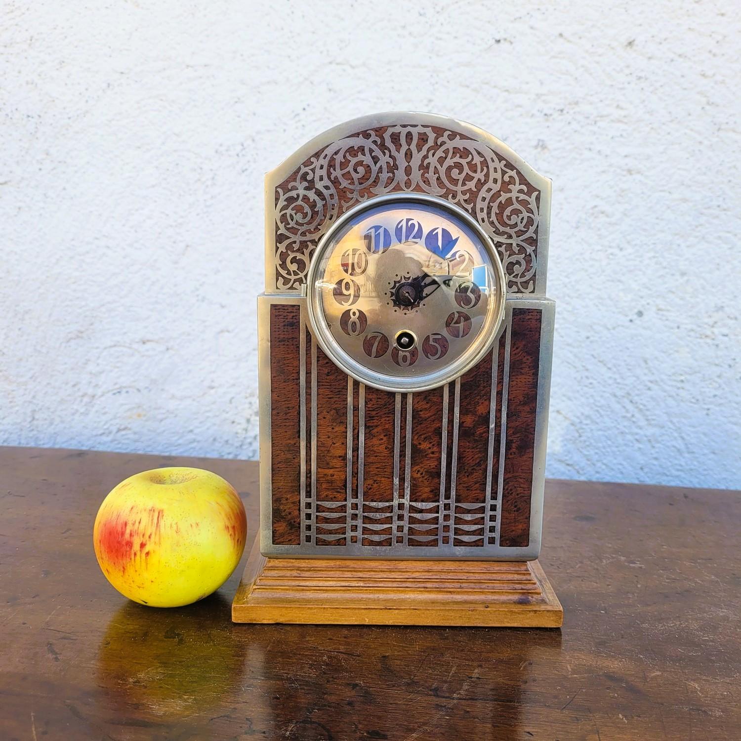 Orologio da tavolo, realizzato in legno di radica e intarsi in metallo che formano un motivo geometrico  

Quadrante con taglio in metallo per segnare i numeri - movimento n°52  

Usuale usura, meccanismo non funzionante.  

Altezza 25 cm
 16.5 x
