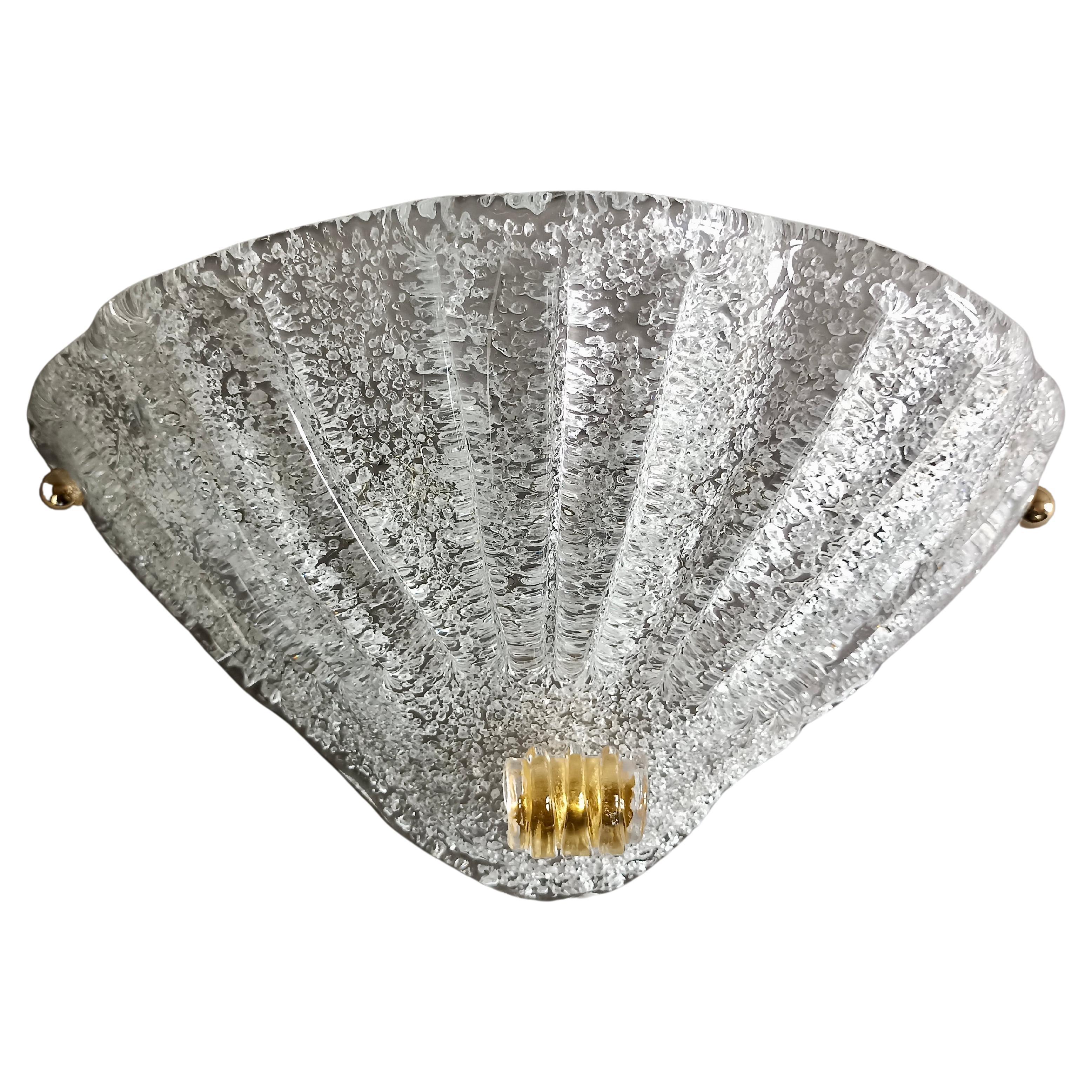 Set of two beautiful sconces from the 1980s, in thick clear Murano glass with a stupendous ribbed workmanship made by hand. 
The surface of the lampshades is smooth glass, while the lower part is made rough by the hot application of minute fragments