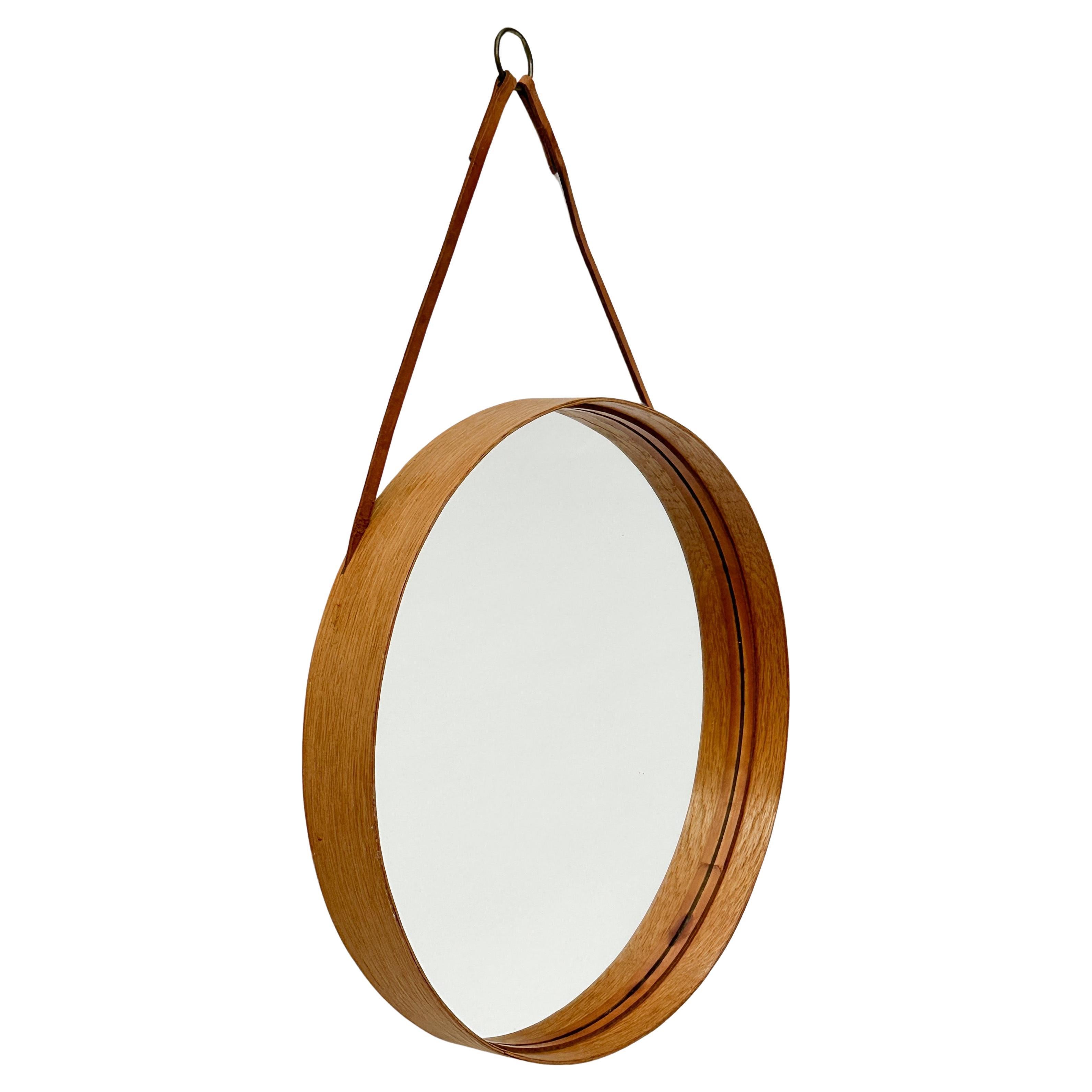 Small swedish mirror designed by Niels Troëd for Glasmäster in Markaryd, Sweden in the 1960s. 

Small size, model No. 101 with a 29 cm diameter. 

Made of a delicate strip of oak wood, lined with a leather band and leather straps with a brass hook.