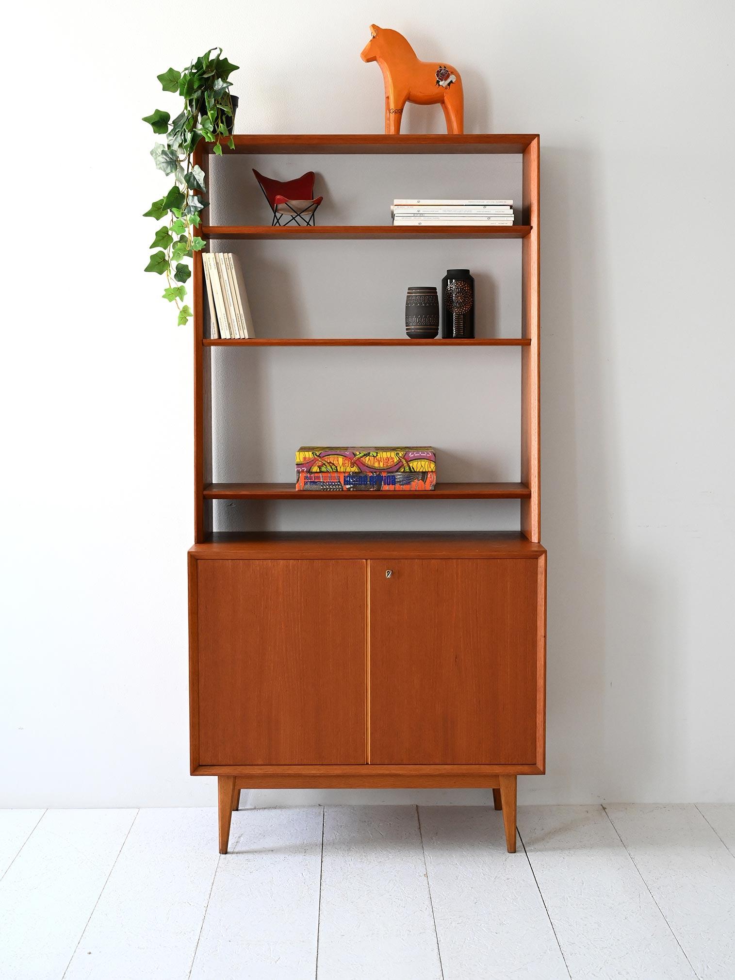 Libreria vintage con struttura in teak, gambe oblique corte, vano chiuso con ante e parte superiore con mensole a giorno.

Libreria scandinava originale degli anni 60 in teak, caratterizzata da gambe oblique e corte, struttura slanciata e