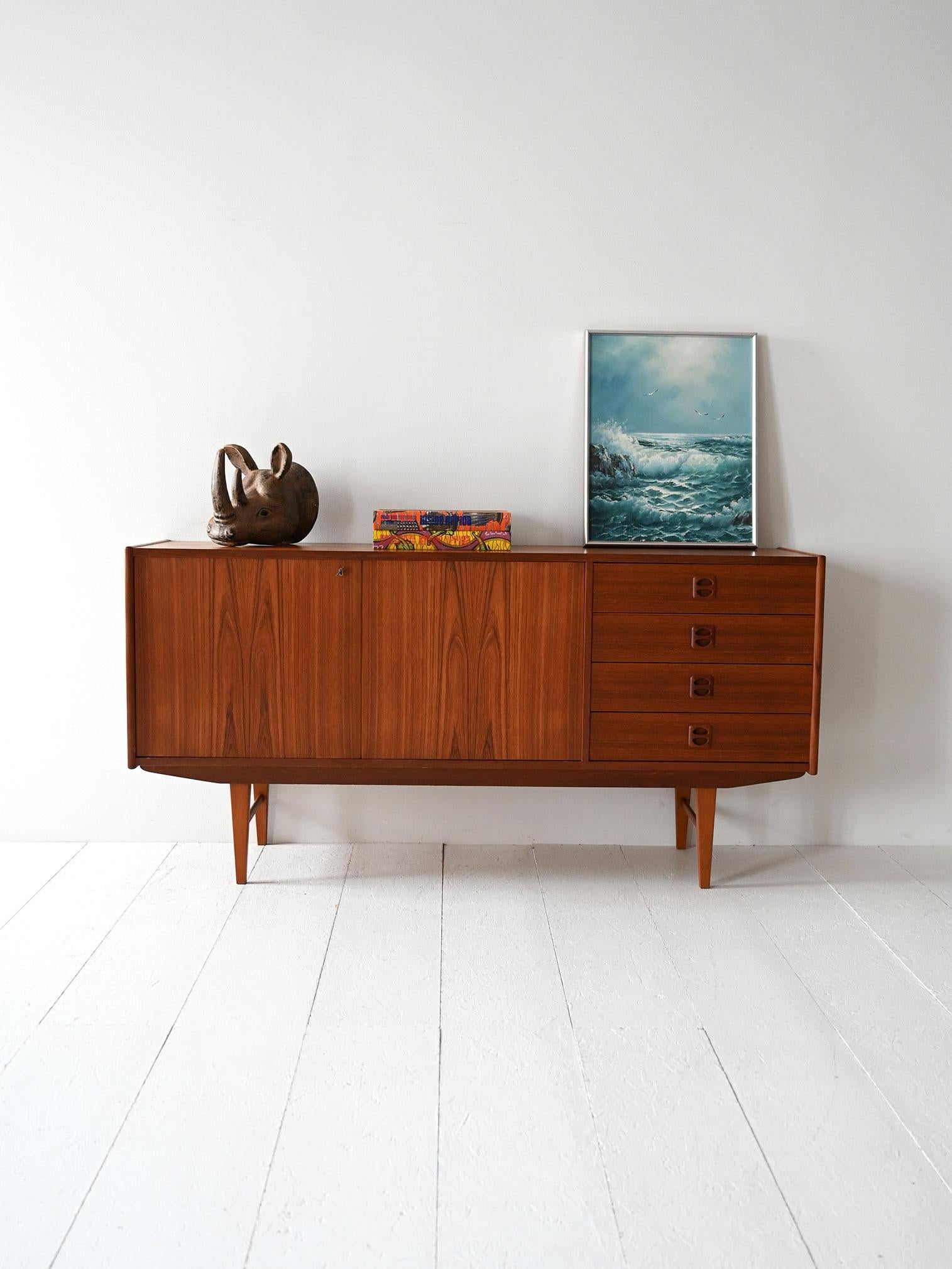 Credenza anni ’50/’60 in teak, quattro cassetti, ante battenti e gambe geometriche affusolate.

Sideboard scandinavo originale in teak, realizzato tra la fine degli anni ’50 e l’inizio dei ’60. Due ante battenti affiancano una colonna di quattro
