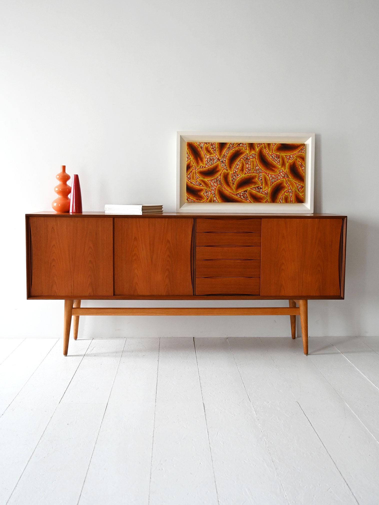 Credenza in teak anni '60 con ante scorrevoli e cassetti a maniglia integrata a gola.

Sideboard scandinavo originale anni '60 realizzato in teak, con gambe in rovere che danno leggerezza alla struttura. È composto da tre ante scorrevoli e una
