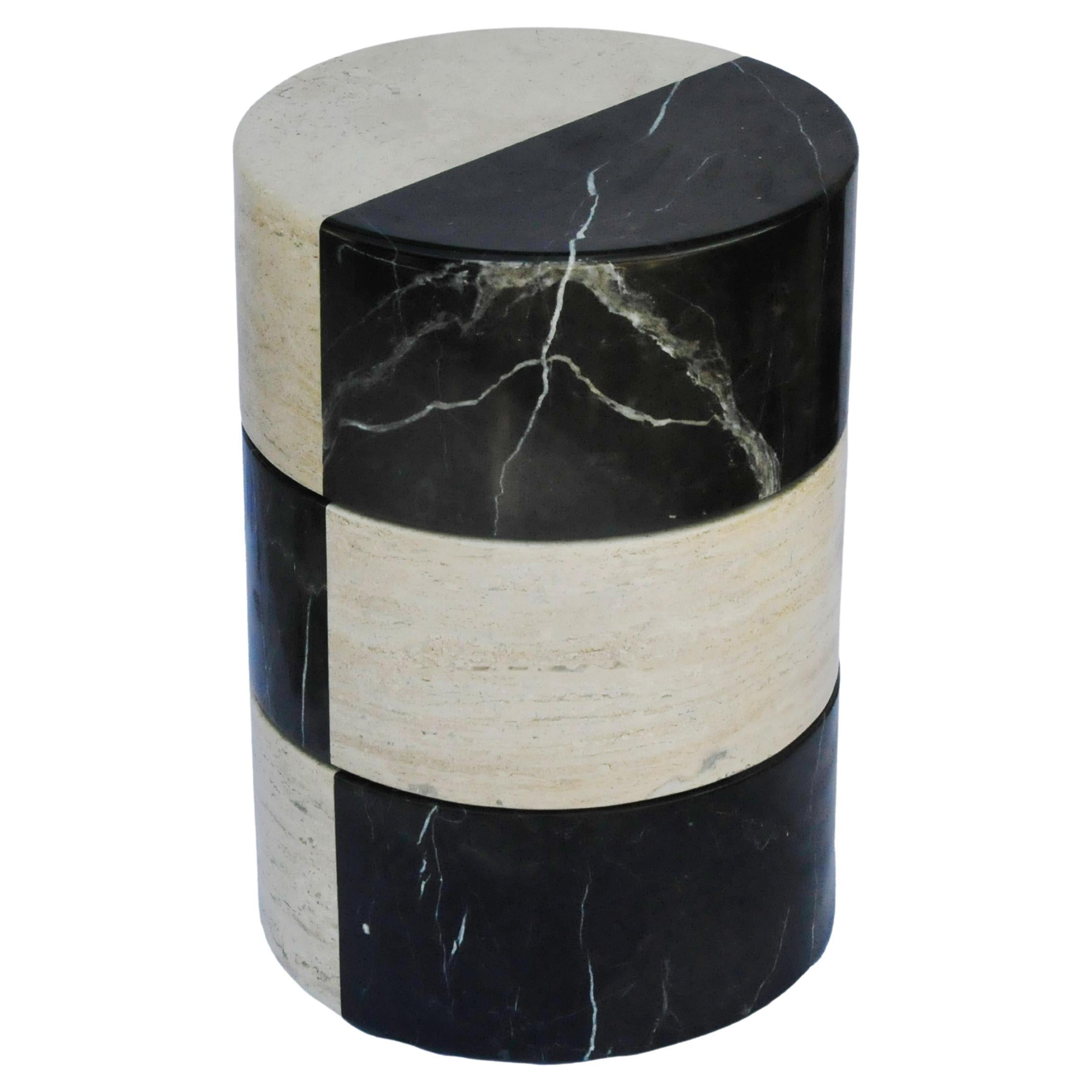 Compuesta de mármol negro y travertino, esta mesa auxiliar contrasta la profunda oscuridad con la cálida neutralidad a través de sus segmentos de piedra varicolor. El objeto se equilibra con una sutil simplicidad en la forma. Esculpida a mano con