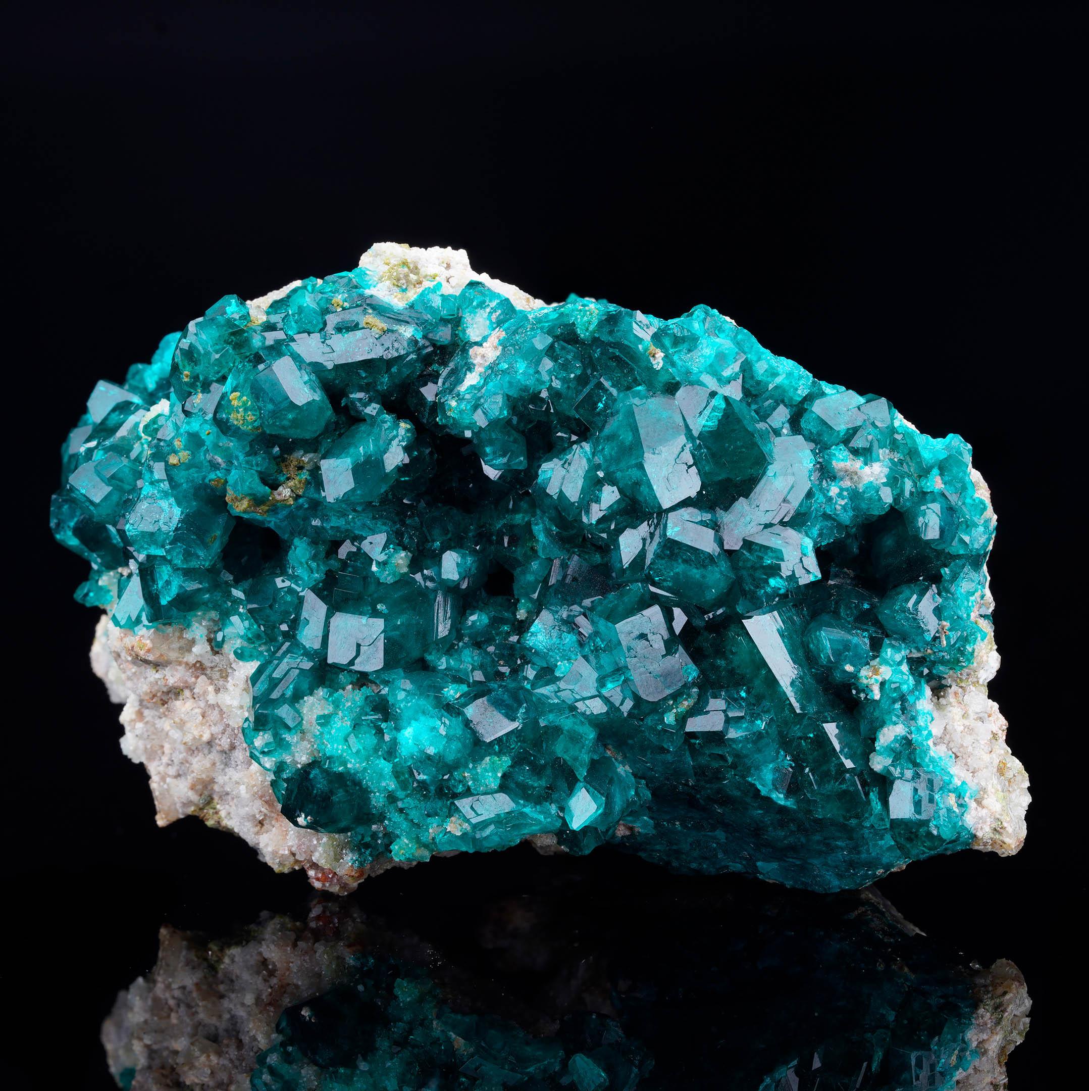 This Dioptase cluster from the legendary Tsumeb Mine in Namibia showcases a dazzling array of saturated emerald-green crystals with exceptional luster and clarity. The sharply terminated Dioptase points radiate across a contrasting light matrix,