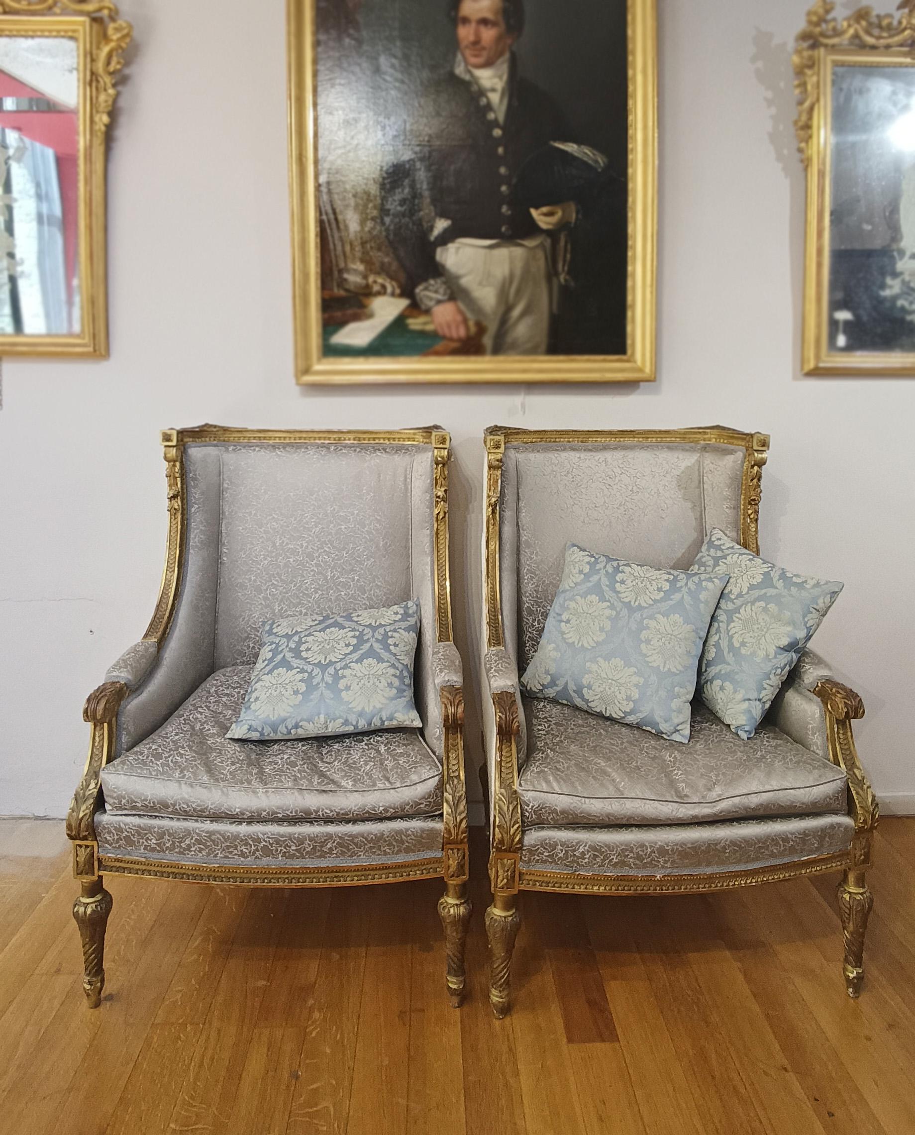 Elegant pair of Bergère armchairs, made of gilded pine wood and finely carved with mastery. The armchairs are decorated on the structure with wood carvings of geometric, scroll and floral motifs, while the legs are turned. They are covered in silver