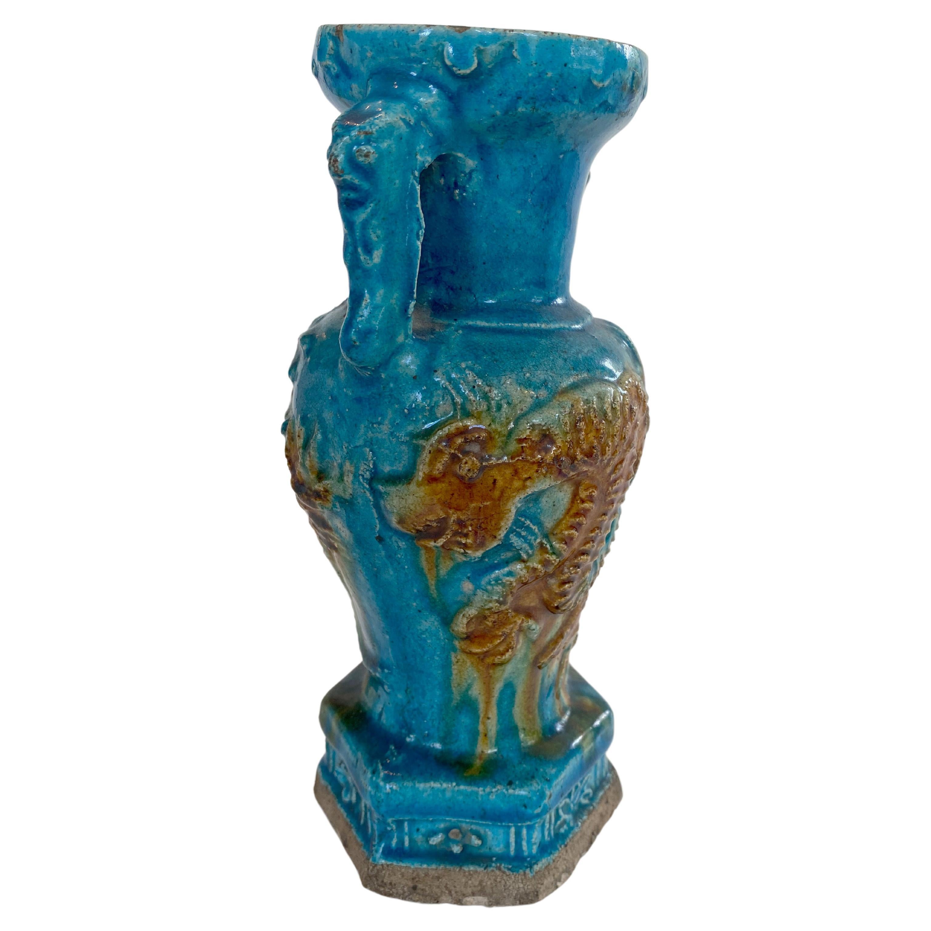 Ming Dynasty (16th century) pottery vase with vivid turquoise glaze, decorated with dragons. The vase is partially moulded, with circular bosses around the mouth rim and a hexagonal base decorated with relief flowers. The vase has two handles that