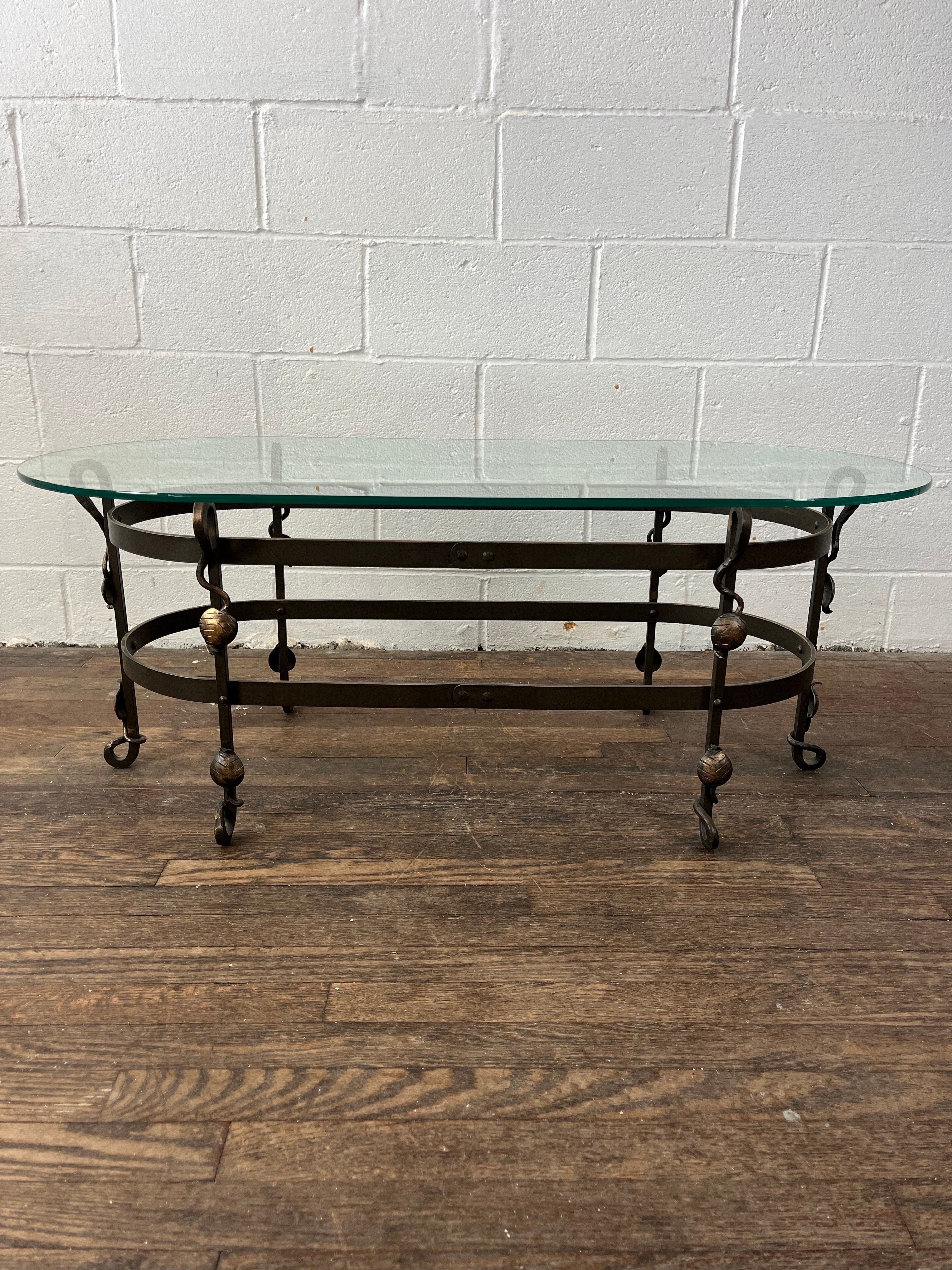 Early 20th Century Arts & Crafts oval coffee table. Original double oval ringed iron base with 6 scrollwork legs with climbing leaf & vine accents. Modern conforming glass top. The base with attractive weathered patina. 