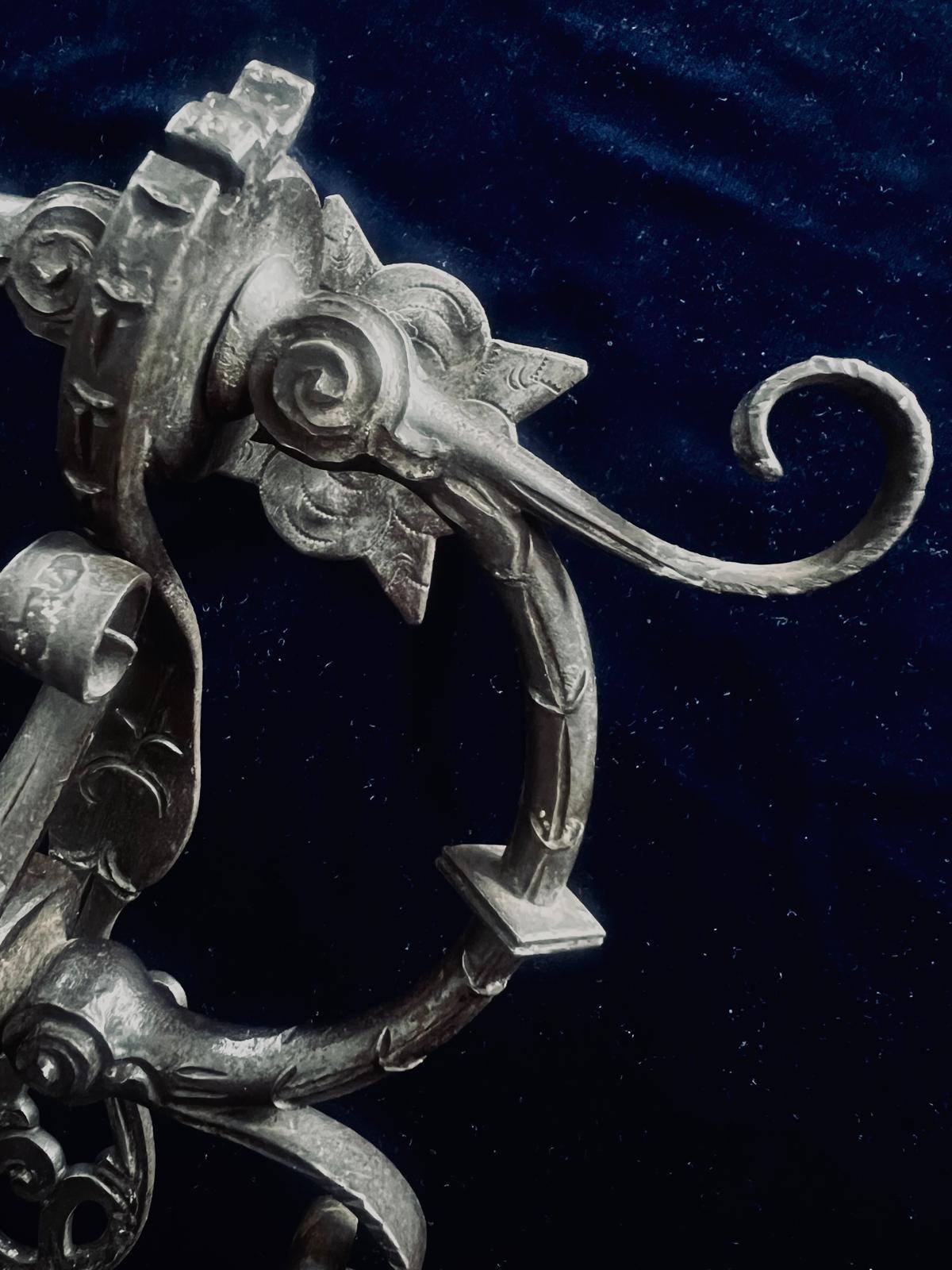 An exceptional and rare 16th century wrought iron door knocker, masterfully hand-forged in the early Renaissance tradition. This striking piece of architectural ironwork is distinguished by its elaborate scroll motifs, symmetrical curled arms, and a