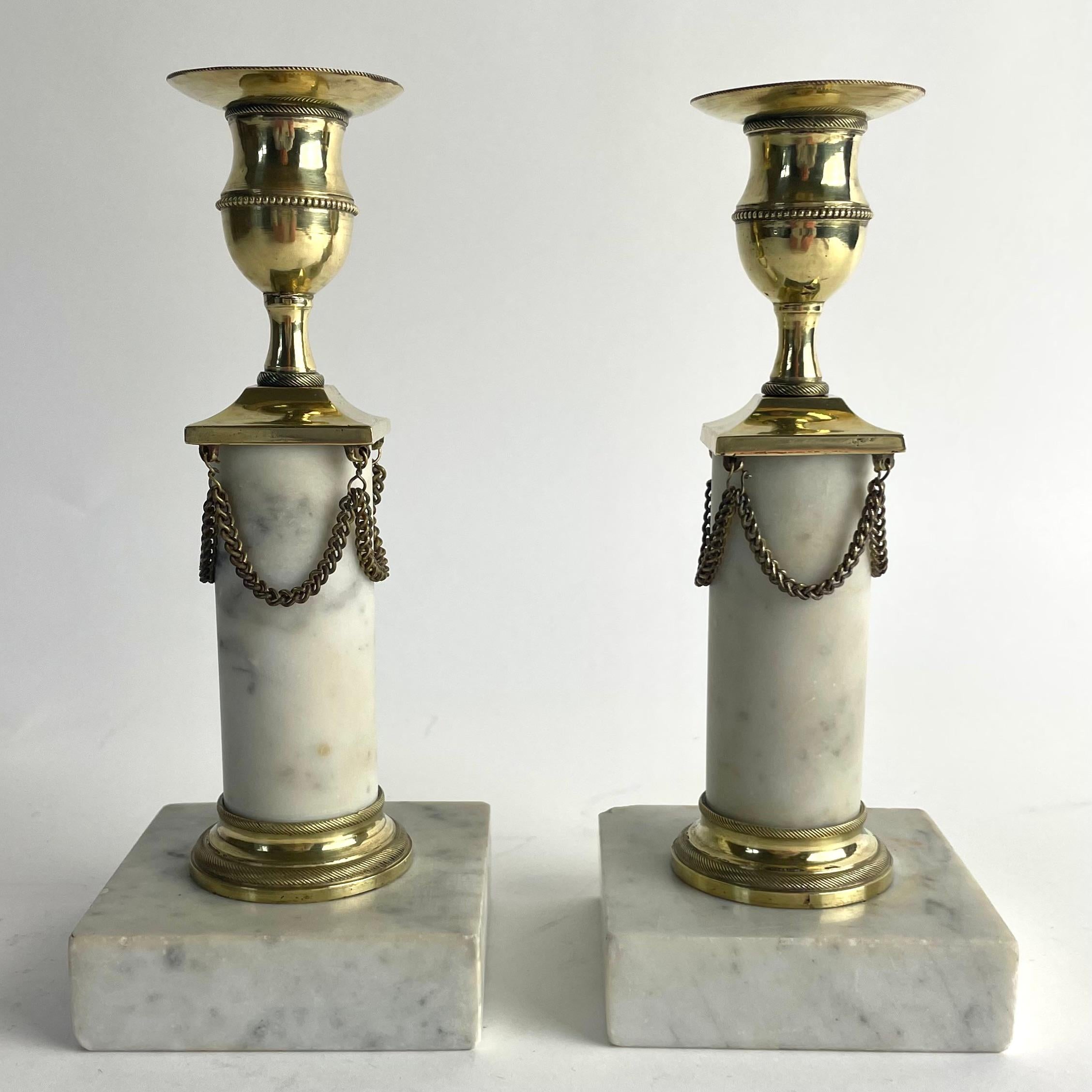 
Pair of Gustavian Candlesticks in Brass and Carrara Marble, Late 18th Century

Elegant pair of Gustavian candlesticks from the 1790s, crafted in brass and fine Carrara marble. The classic columnar design is complemented by original draped chains