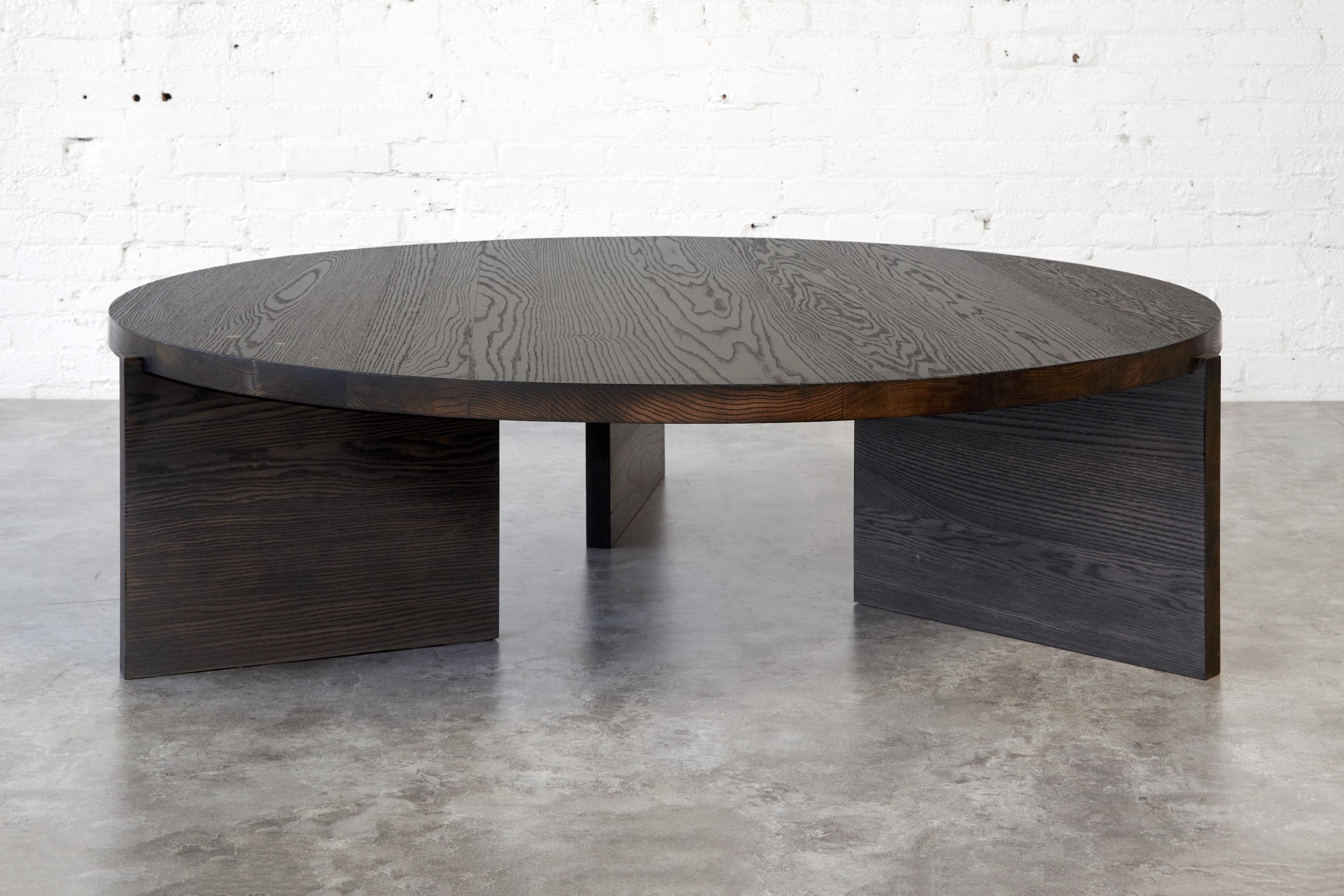 Table basse ronde en chêne torréfié avec une légère finition à l'huile et à la cire d'onyx argenté. Les pieds de la table sont légèrement décalés pour ajouter un effet dramatique. Cette table basse ronde en bois massif comprend une grappe de pièces