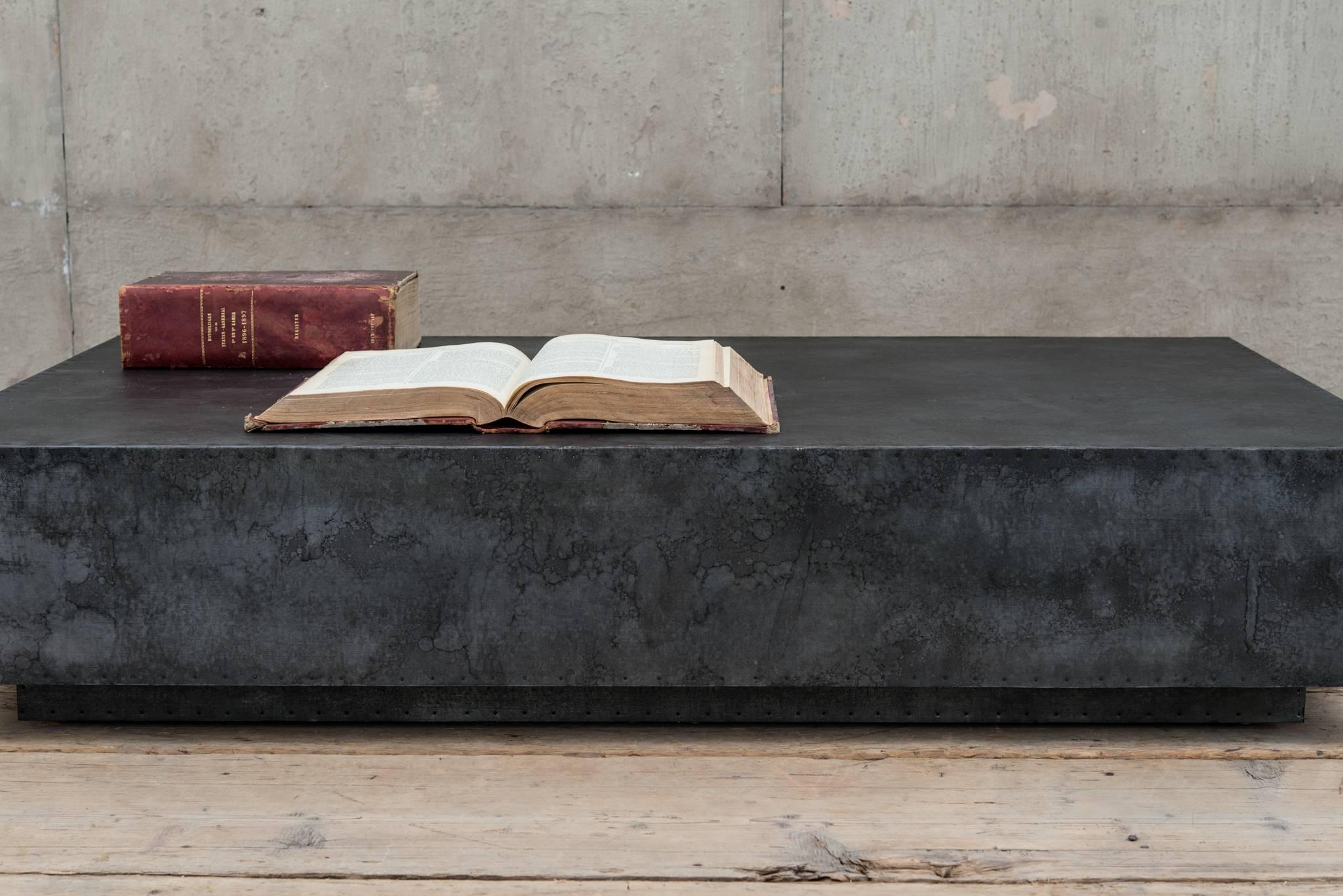 Zinc covered coffee table on plinth.
A sleek slab of zinc floats over a recessed plinth. Antiqued patina and spit-tack detailing add age and character to this modernist piece.