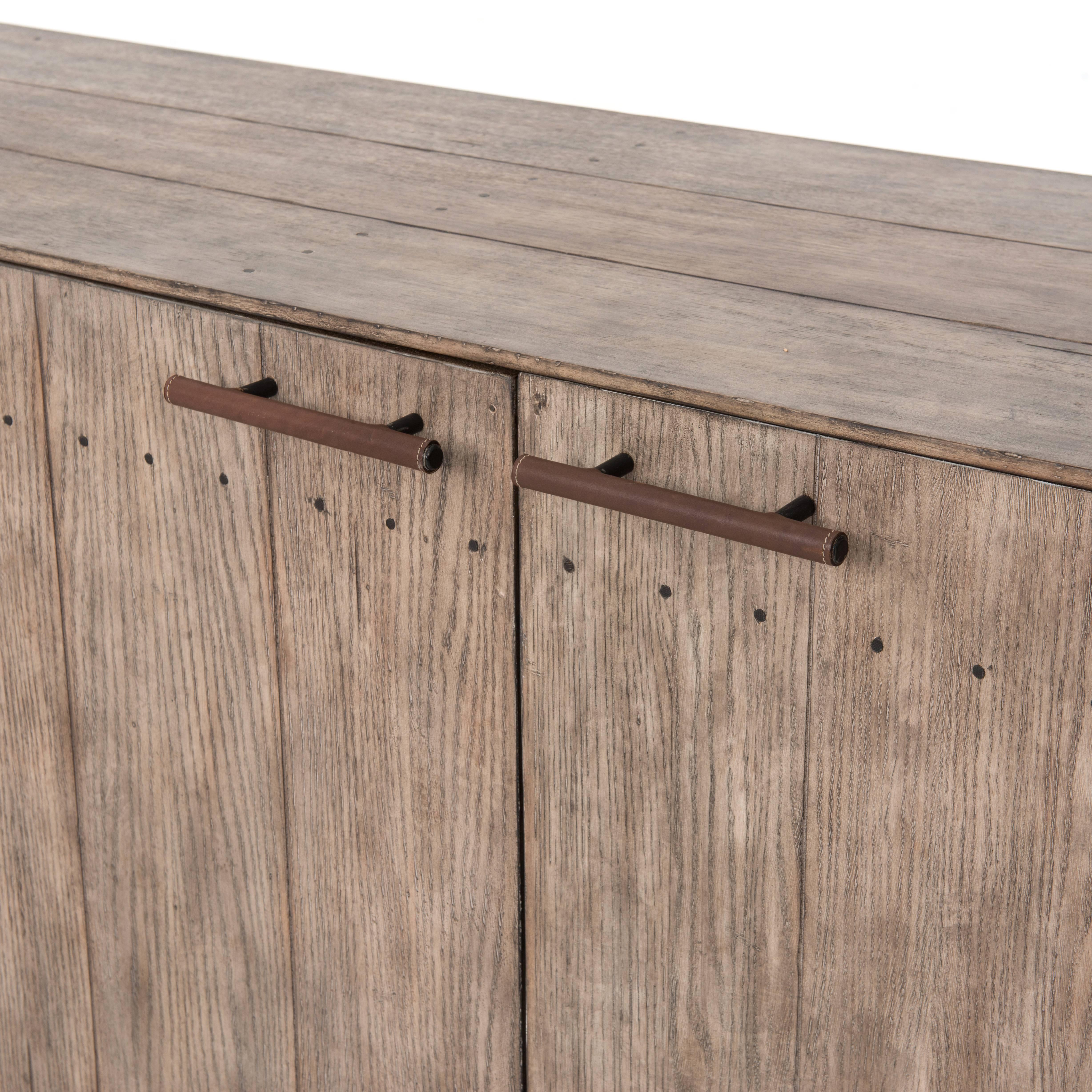 Distressed oak is washed and softened to a driftwood grey, and accented by leather-wrapped iron hardware. Long narrow sideboard.