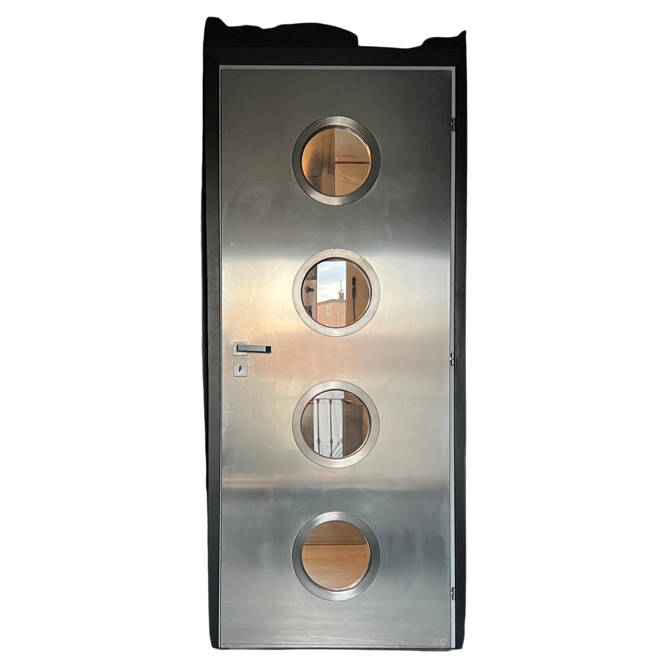 Puerta metálica contemporánea de acero inoxidable hecha a medida con ojos de buey redondos, diseñada por Spinzi y fabricada en Italia.

Inspirada en las obras de Jean Prouvé, esta puerta se construye a partir de una puerta de madera normal