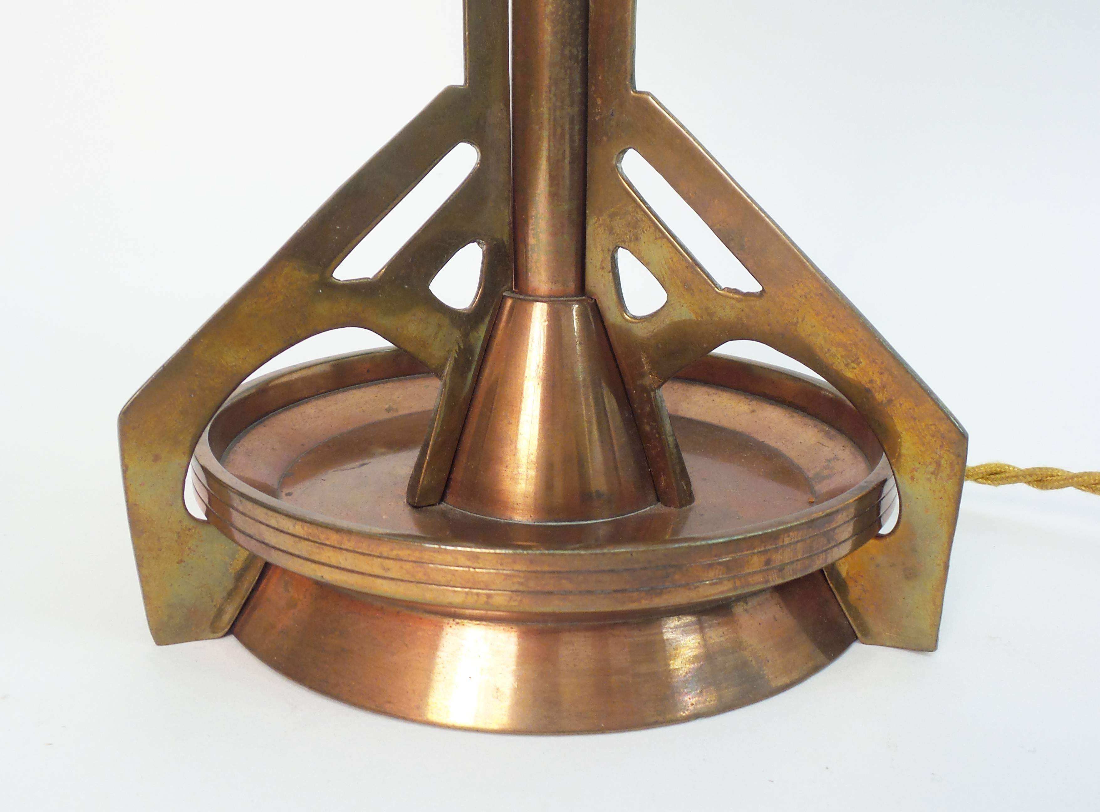 A Jugendstil period table lamp of unusual design executed in brass and copper, the frosted glass shade resting in a pierced brass frame lined in silk.