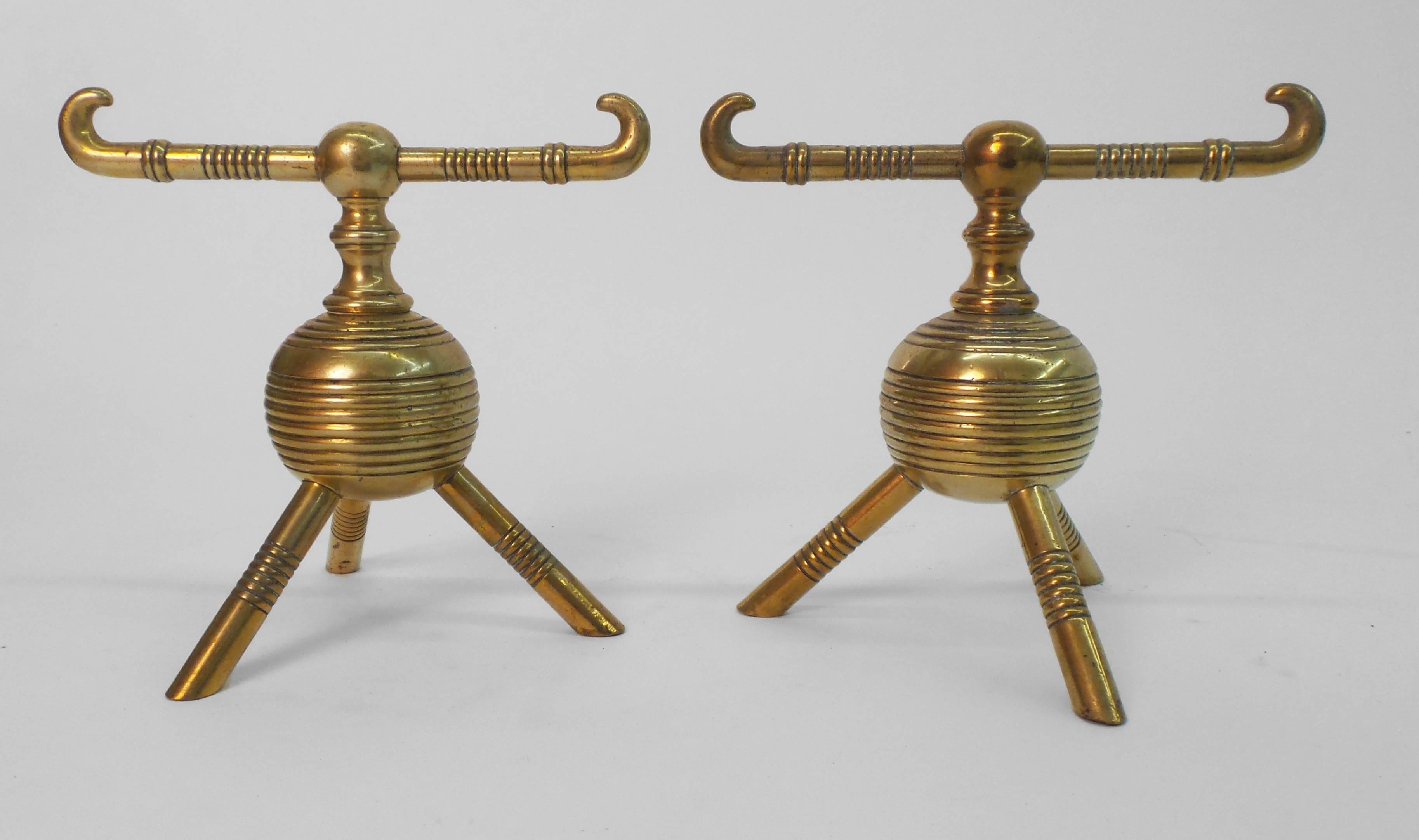 A pair of English, Aesthetic period brass fire dogs having ribbed bodies supported on three feet. Design attributed to Dr. Christopher Dresser made by Benham & Froud, circa 1890.