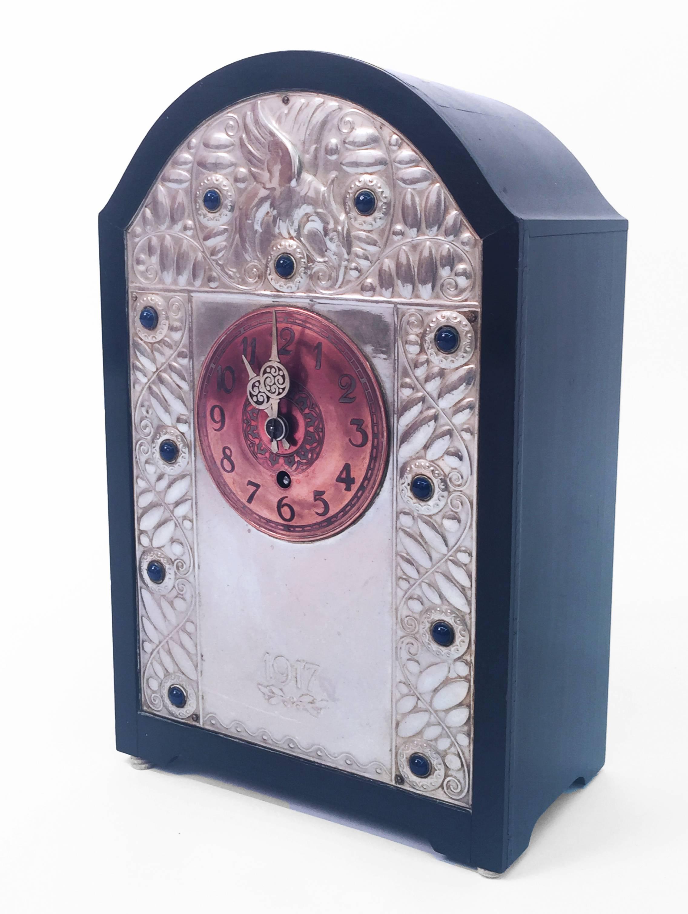 A Secessionist period Viennese mantel clock in the manner of the Weiner Werkstätte having an ebonized case and an exquisitely detailed copper dial mounted on a silver face plate, repousse decorated with leaves, tendrils, an eagle, and dark blue