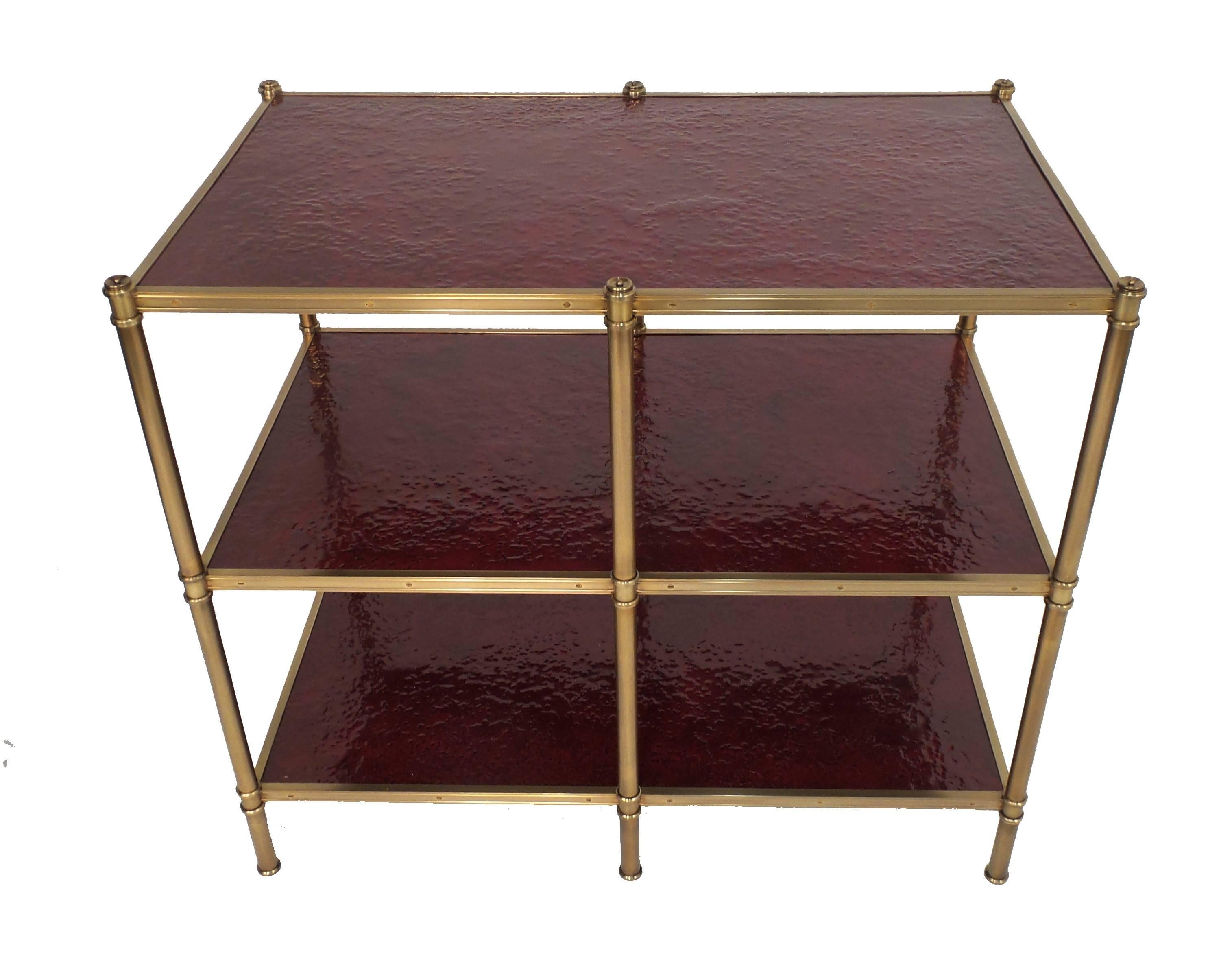 A custom low bookcase, or sofa table, version of the étagère designed by Frederick Victoria for Billy Baldwin's client Cole Porter with three shelves having a textured surface in crimson molten gypsum finish, in a patinated brass frame. Custom