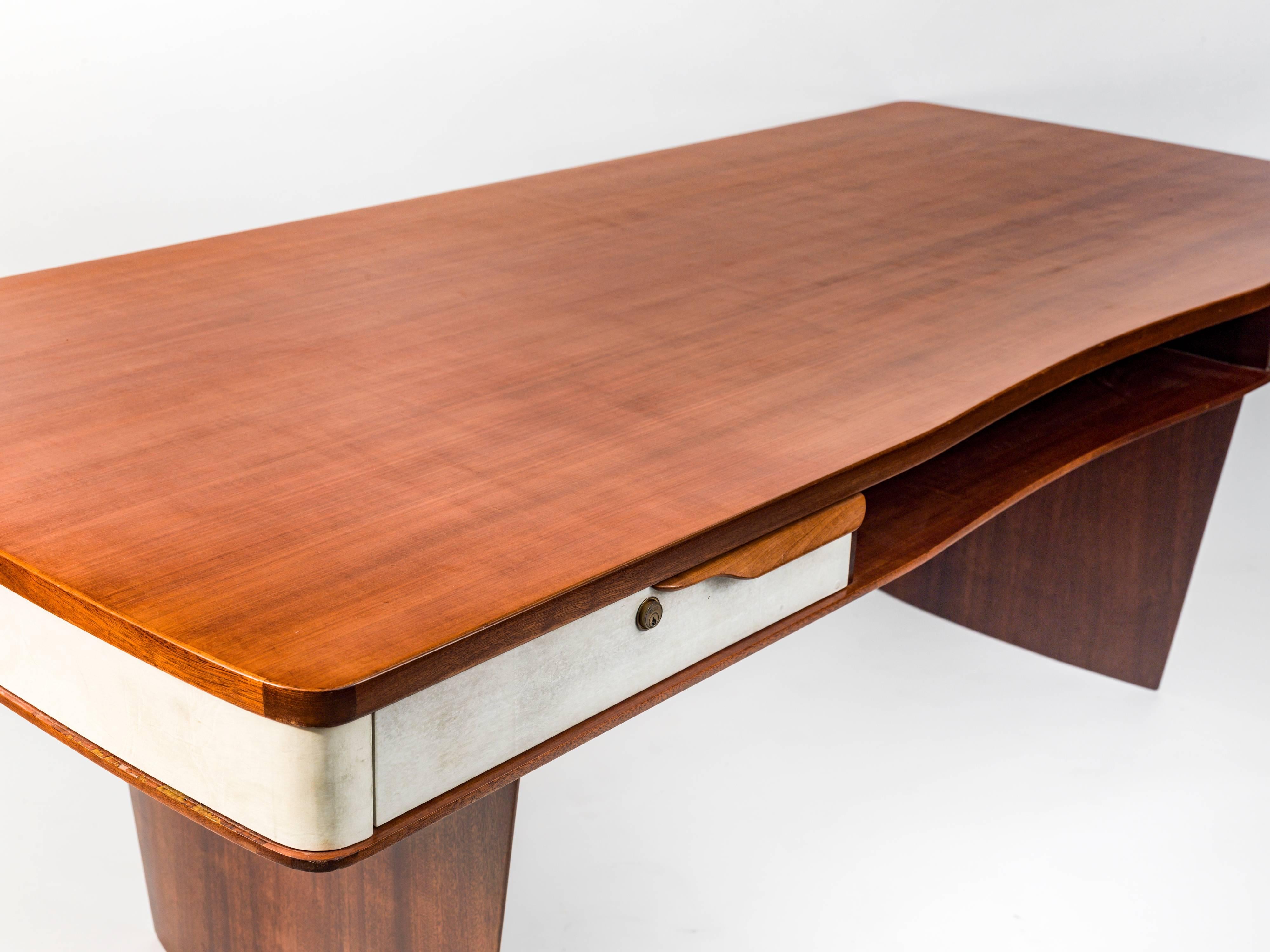 A modernist design desk having two drawers and central storage areas front and back. Executed in mahogany with parchment details on drawer fronts and around the entire apron, Italian, circa 1955.