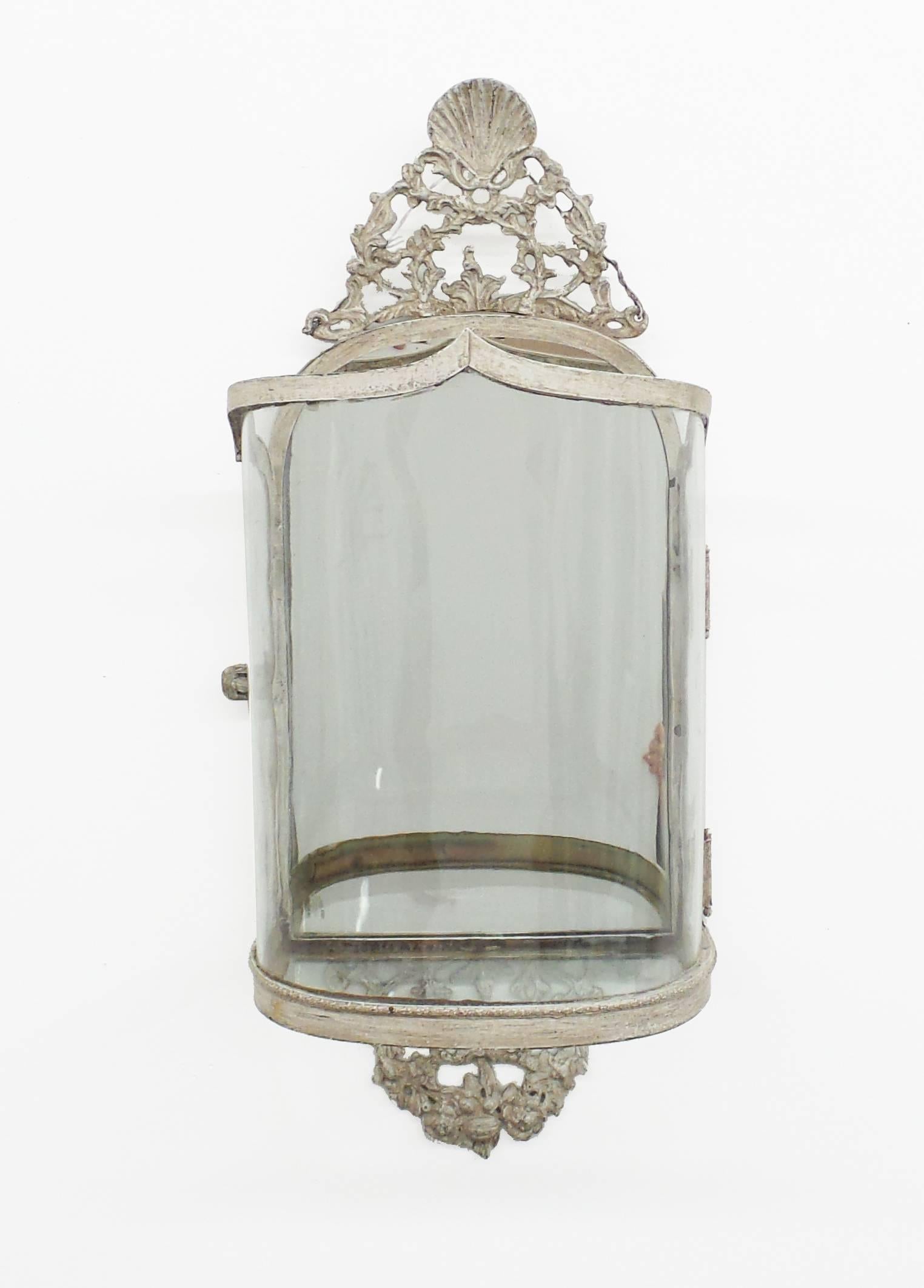 A Queen Anne style wall lantern executed in brass with a handcrafted slumped glass shade and antiqued mirror back. Candelabra not included. Can be electrified. Brass and painted finished available. Overall dimensions 11” wide x 27” high x 7.5