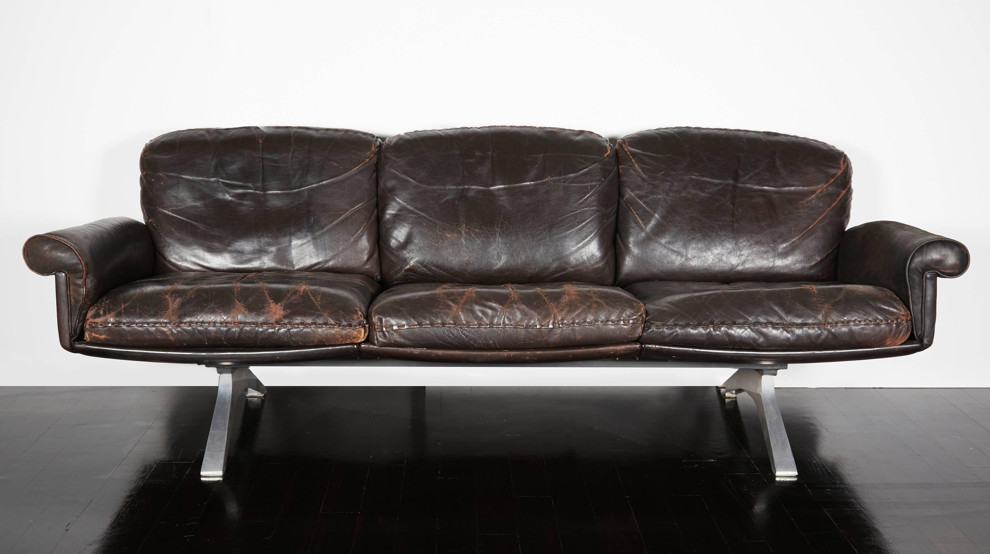 A dark brown leather sofa by DeSede with nice patina, rolled arms, six cushions with whipstich edge detail and a brushed metal base.
Excellent vintage condition.
