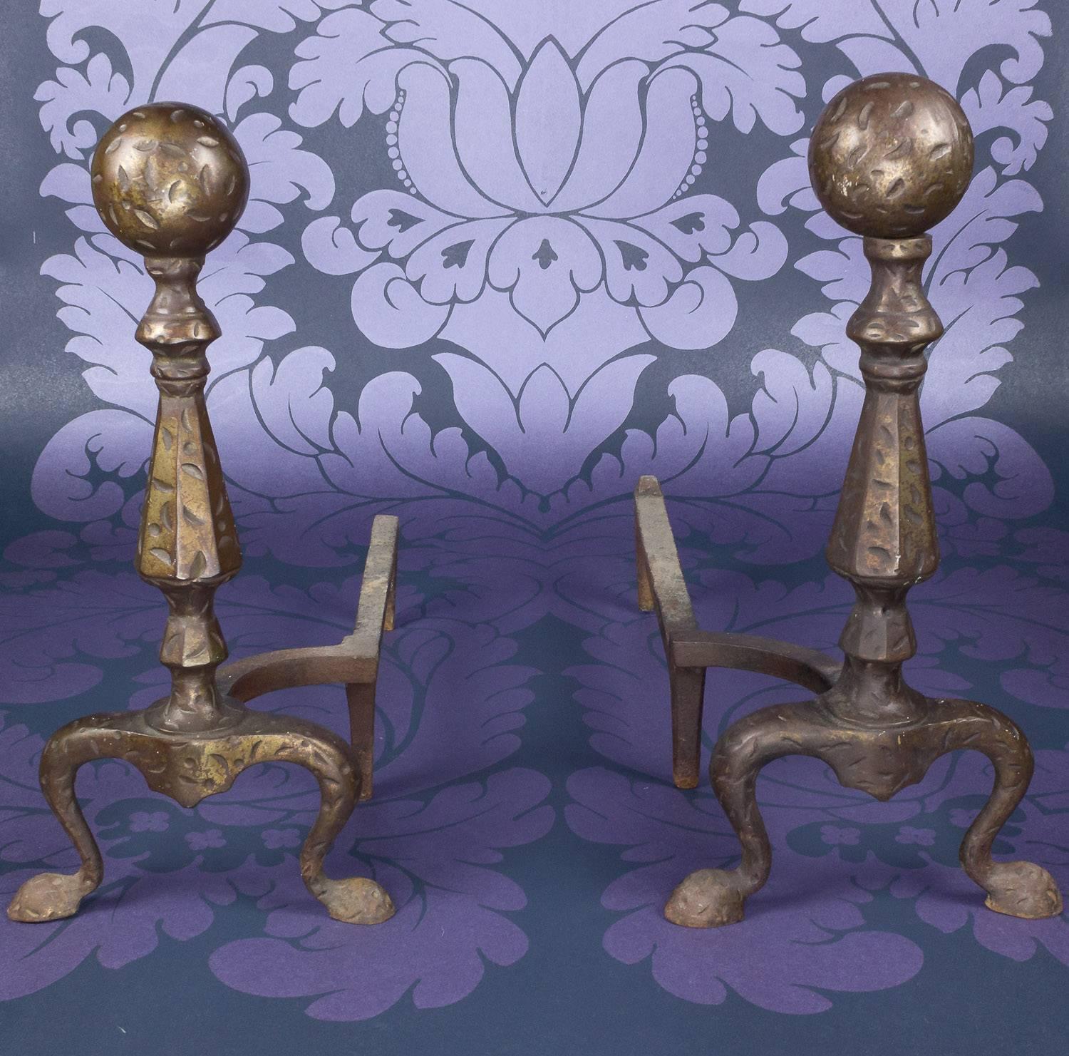 The pair of patinated and hammered iron andirons from 145 Antiques is a charming testament to the American craftsmanship of the early 20th century. With a classic design set on scrolled feet and a raised ball finial, these andirons radiate elegance