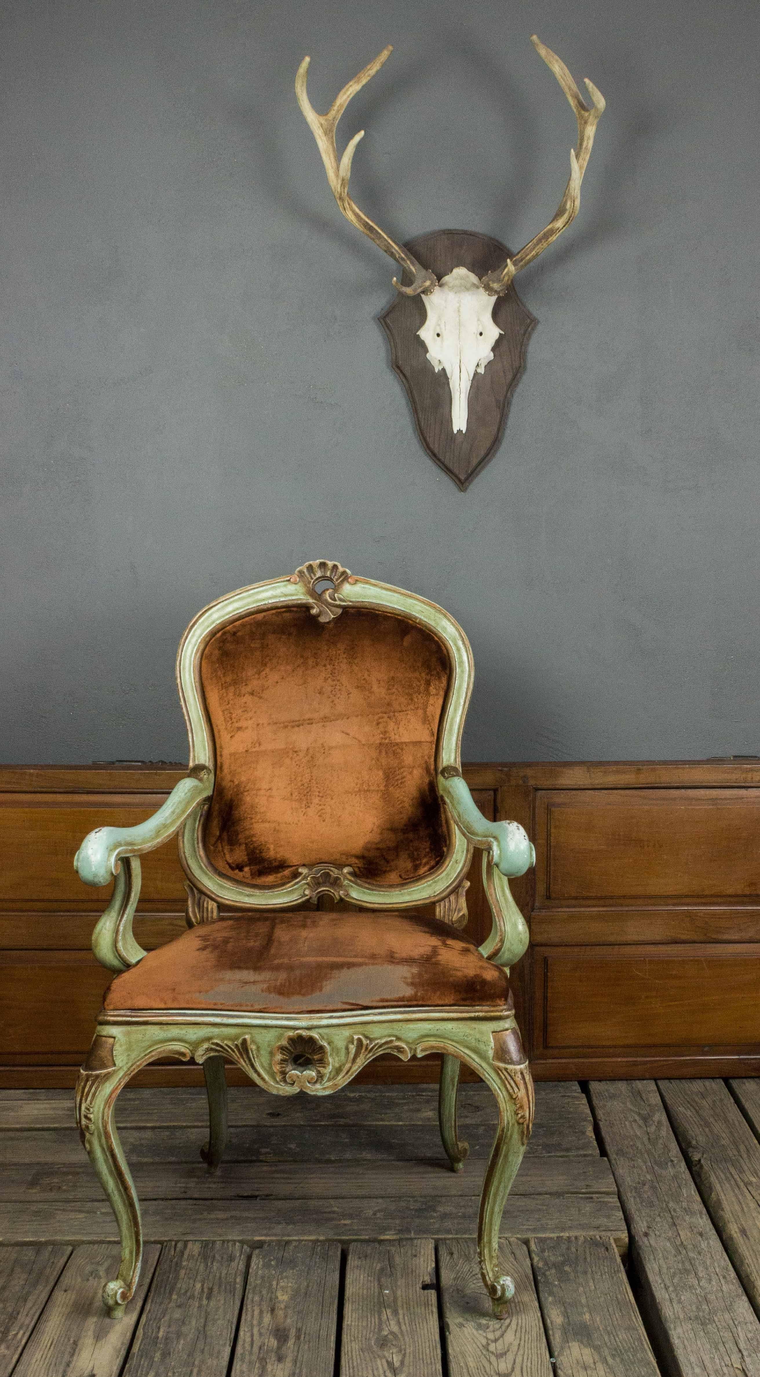 This elegant 1920s Venetian style armchair is an example of classic beauty that will become the centerpiece of any space. The wooden frame is painted in dreamy shades of green and gold with an aged patina, giving it an antique, regal quality. The