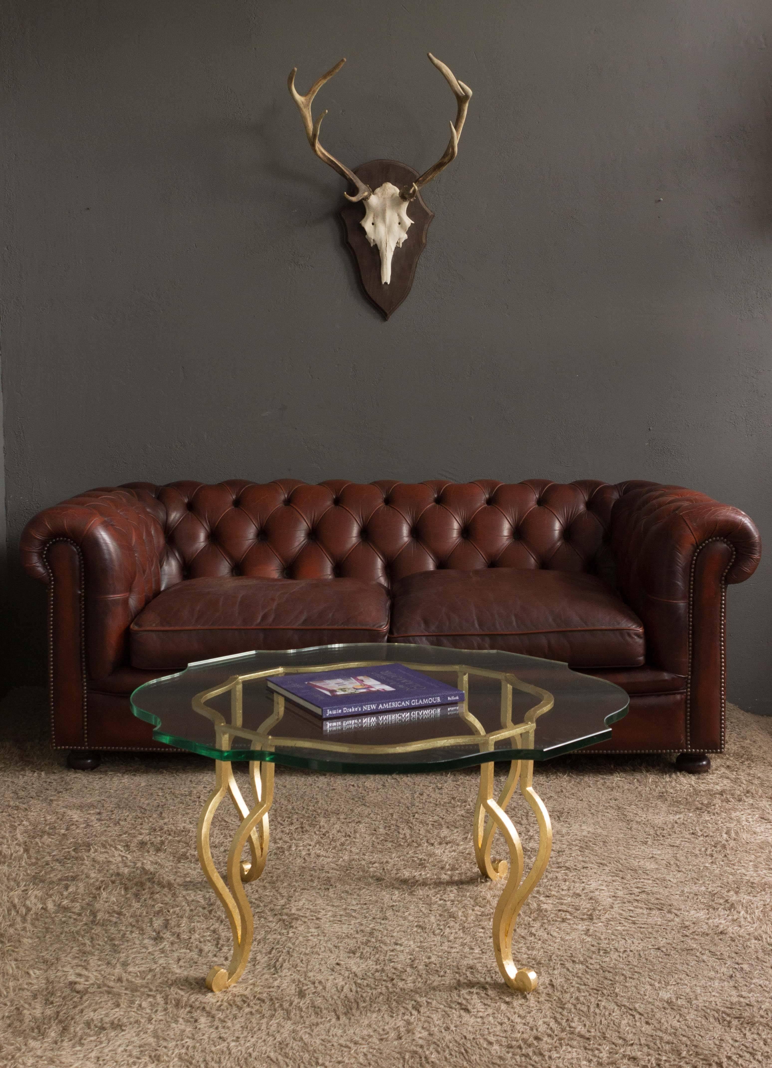 A stunning Italian 1940s gilt iron coffee table with a custom clear glass surface. Add a touch of luxury to your living room with this ornate Italian gilt iron coffee table from the 1940s. The intricate details and the gilt finish give this table an