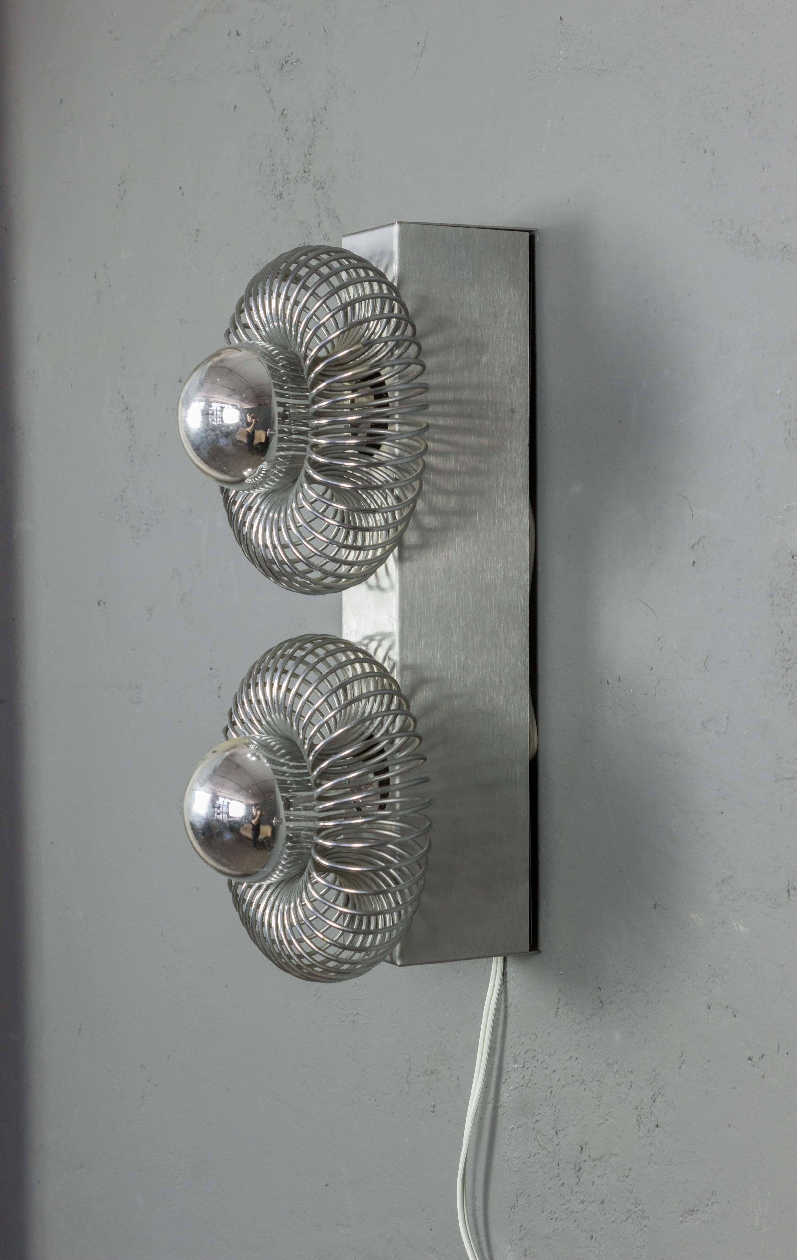 French, 1970s metal sconce with double lights. The exposed and silvered bulbs are surrounded by expandable metal enclosures of connected rings.
