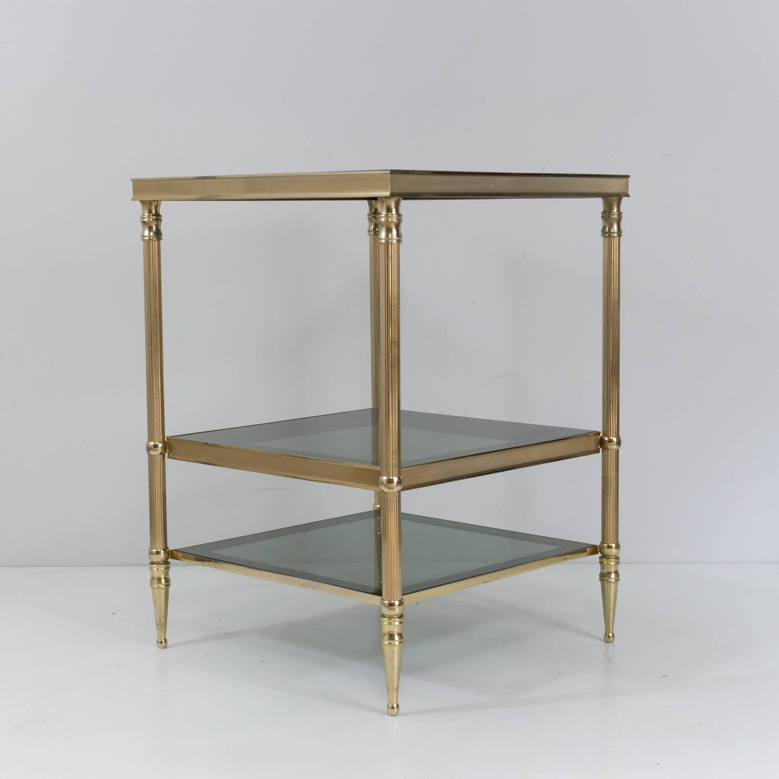 Handsome pair of three-tiered brass side tables with glass shelves. In the style of Maison Jansen. French, 1960s.

These side tables are currently in France, please allow 2 to 4 weeks for delivery. Shipping to our warehouse in New York is included