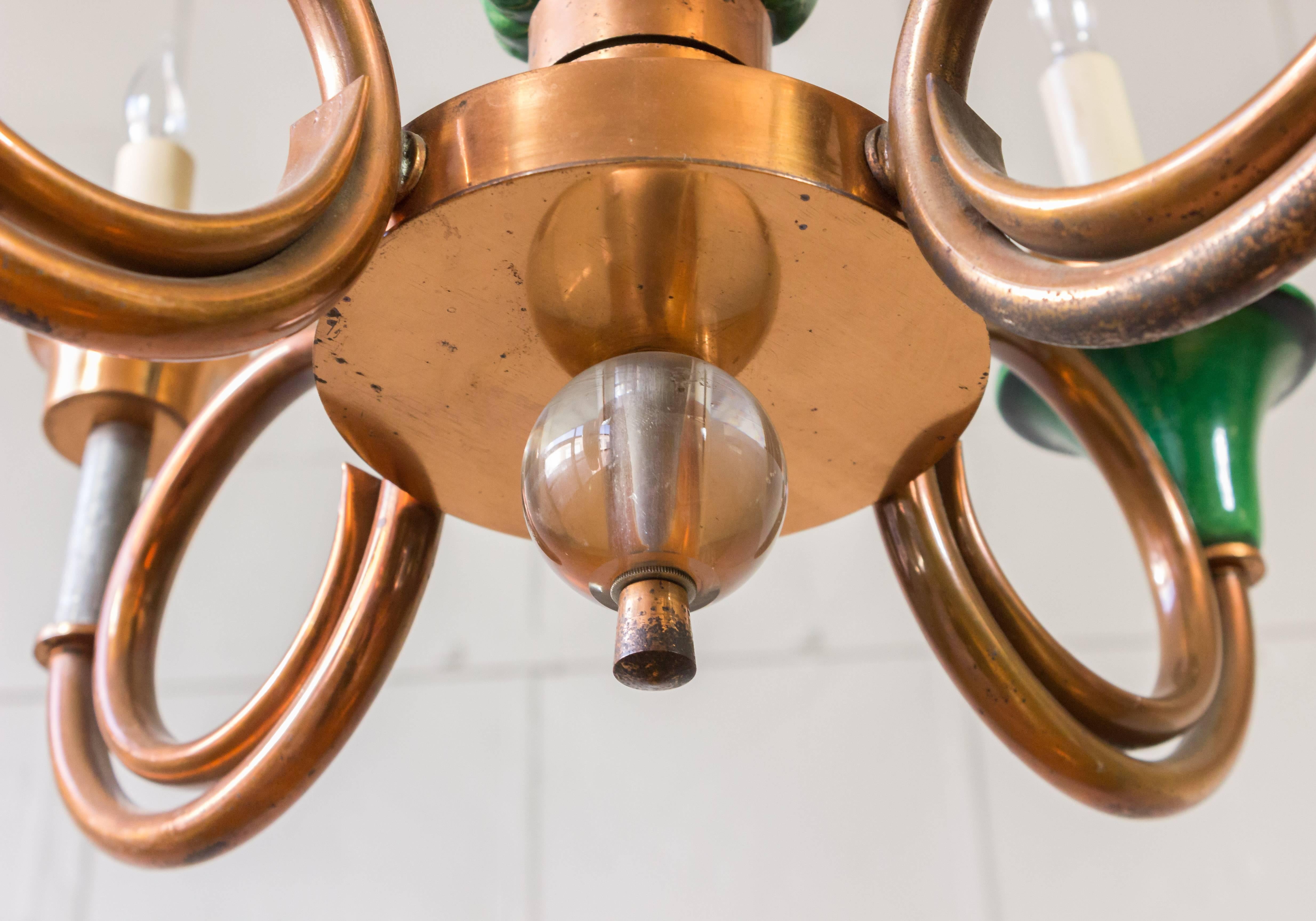 This French chandelier from the 1940s is a stunning amalgamation of green ceramic and copper. It features four arms that extend gracefully from the centerpiece, making it a truly unique and original piece. The design echoes European chic and