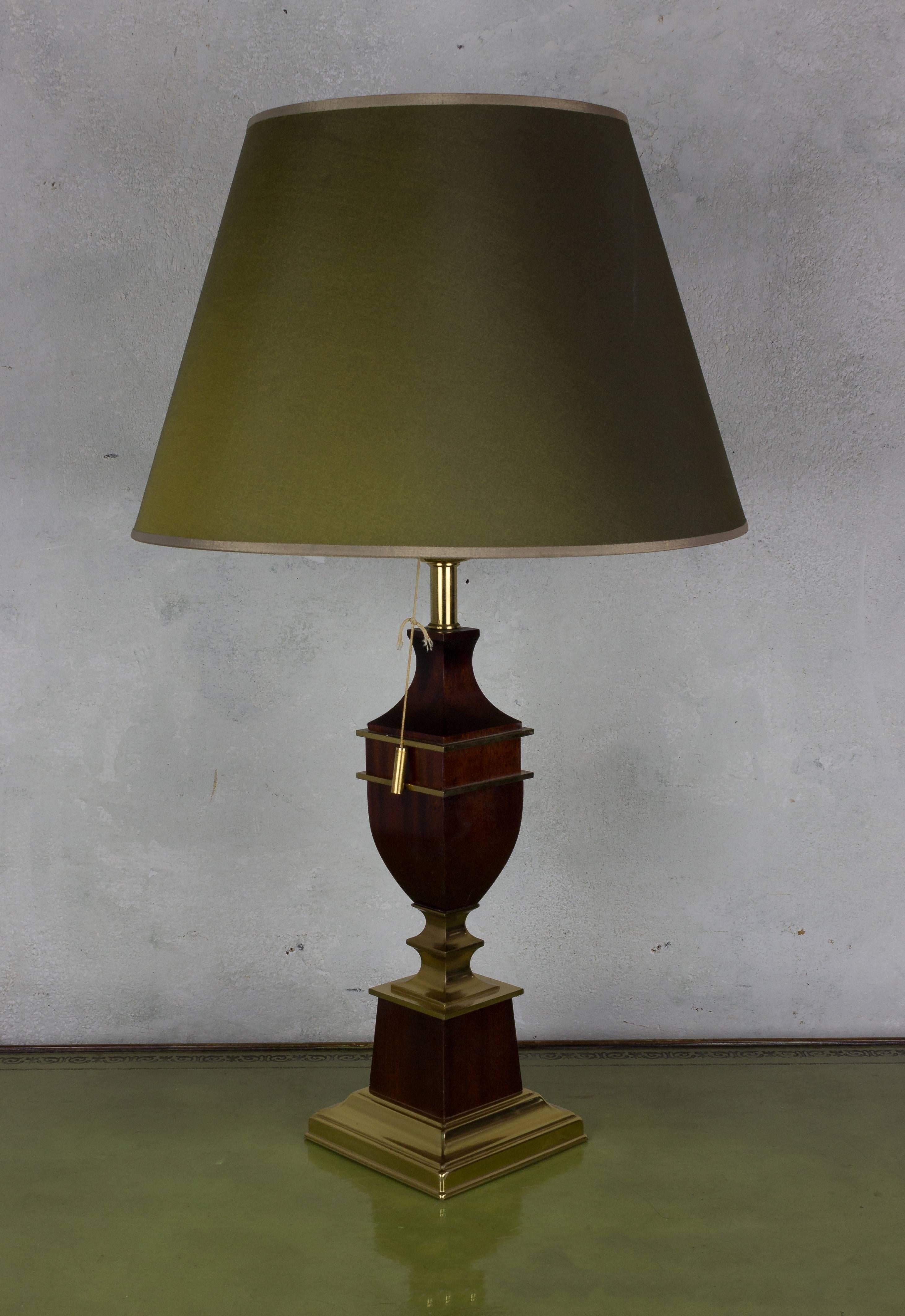 A handsome neoclassical style table lamp in the form of an urn. The lamp is made of mahogany wood with brass trim, and mounted on a brass base. The original green shade is European style and does not require a harp. The lamp takes a single light