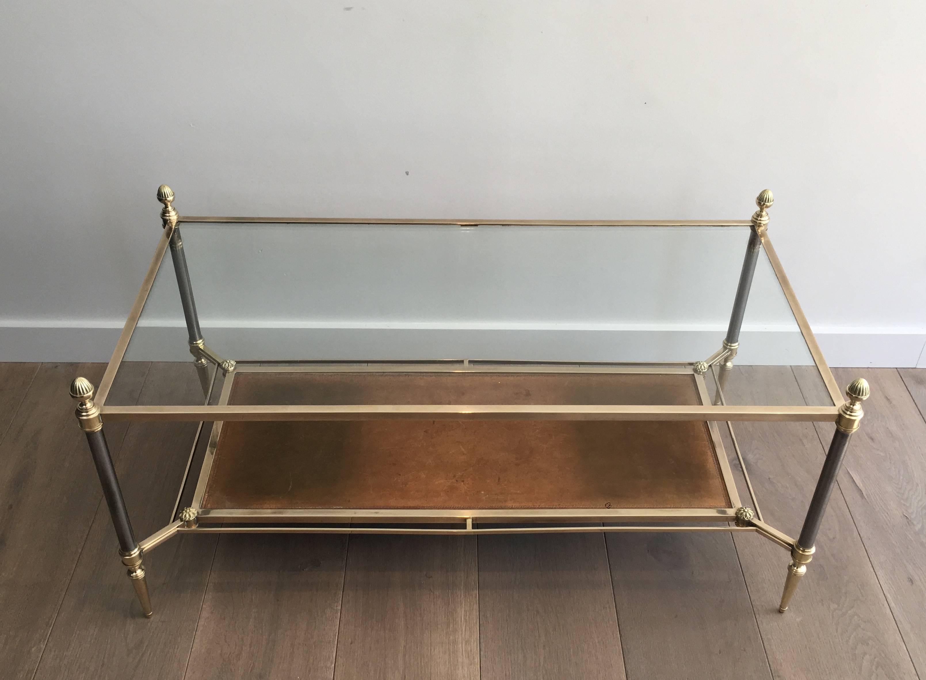 Beautiful neoclassical style brushed steel and brass coffee table with clear glass top shelf and brown leather on the bottom. The vintage leather has variations most likely caused by sun bleaching. The table frame is polished brass with darker