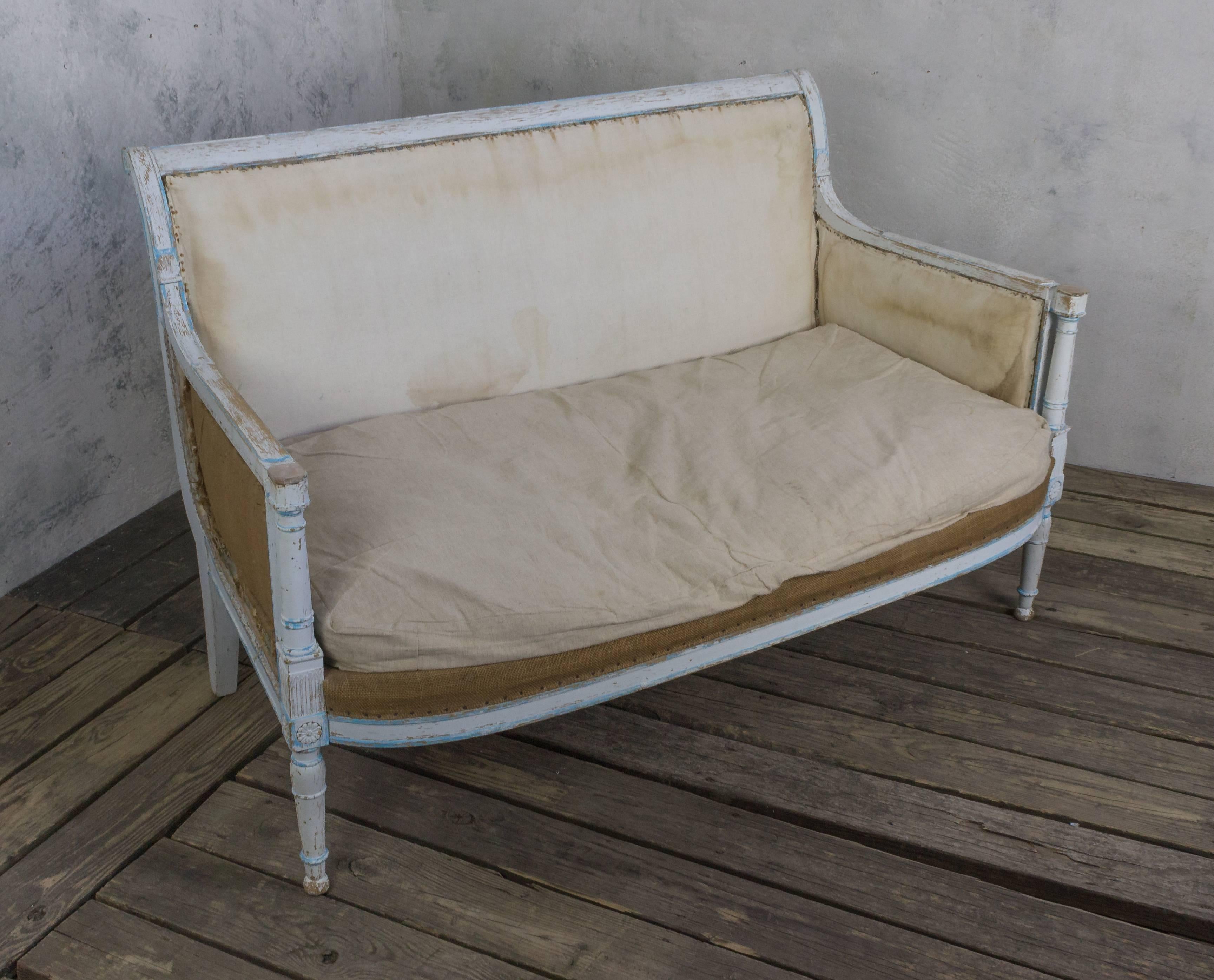 An exceptional French mid 19th century settee in the Directoire style. This settee is a beautiful piece of furniture. The wooden frame still has traces of the original blue-painted decoration over its white patina, and it boasts a loose seat