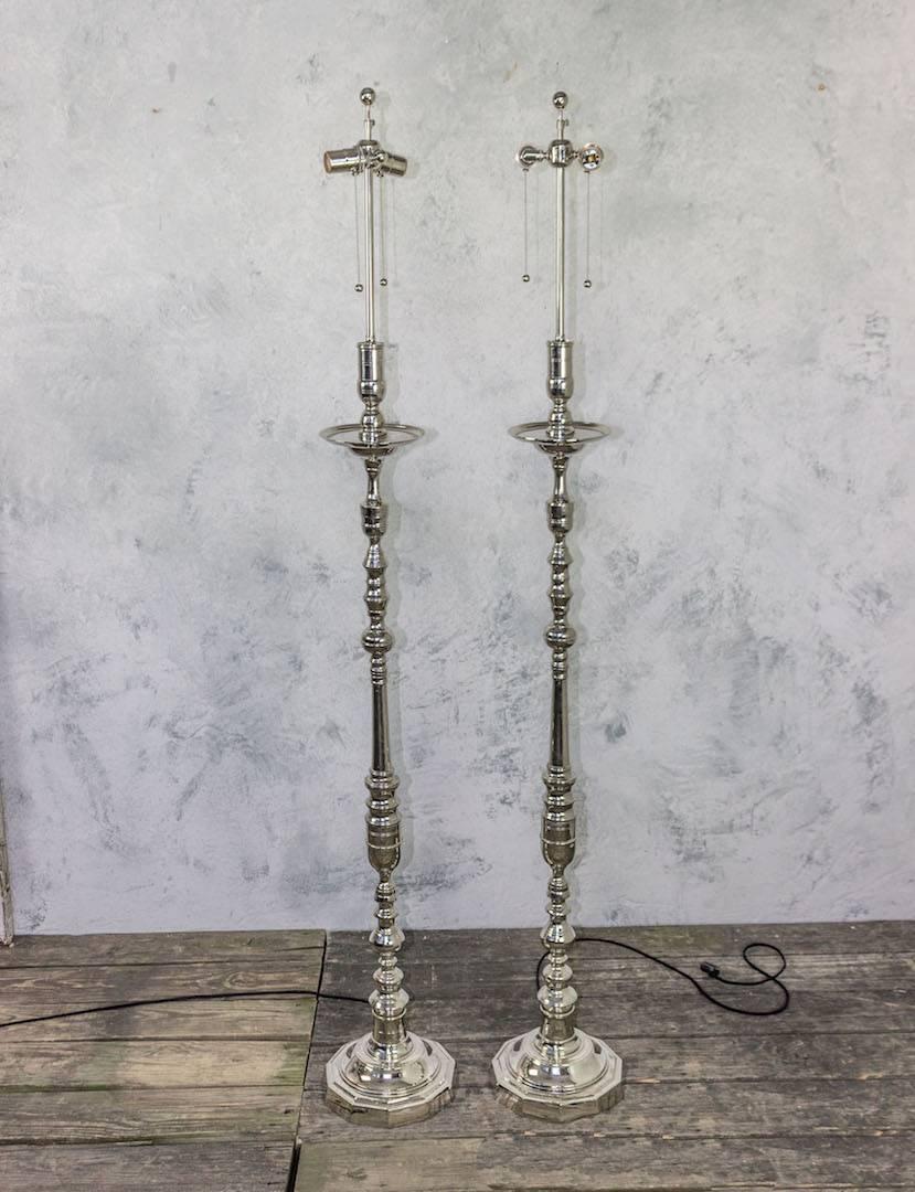 Introducing a stunning pair of French 1940s nickel plated floor lamps, featuring ornate stems made up of turned and cast bronze and brass components that gracefully guide the gaze toward their elegant bobeches. These lamps are in very good vintage